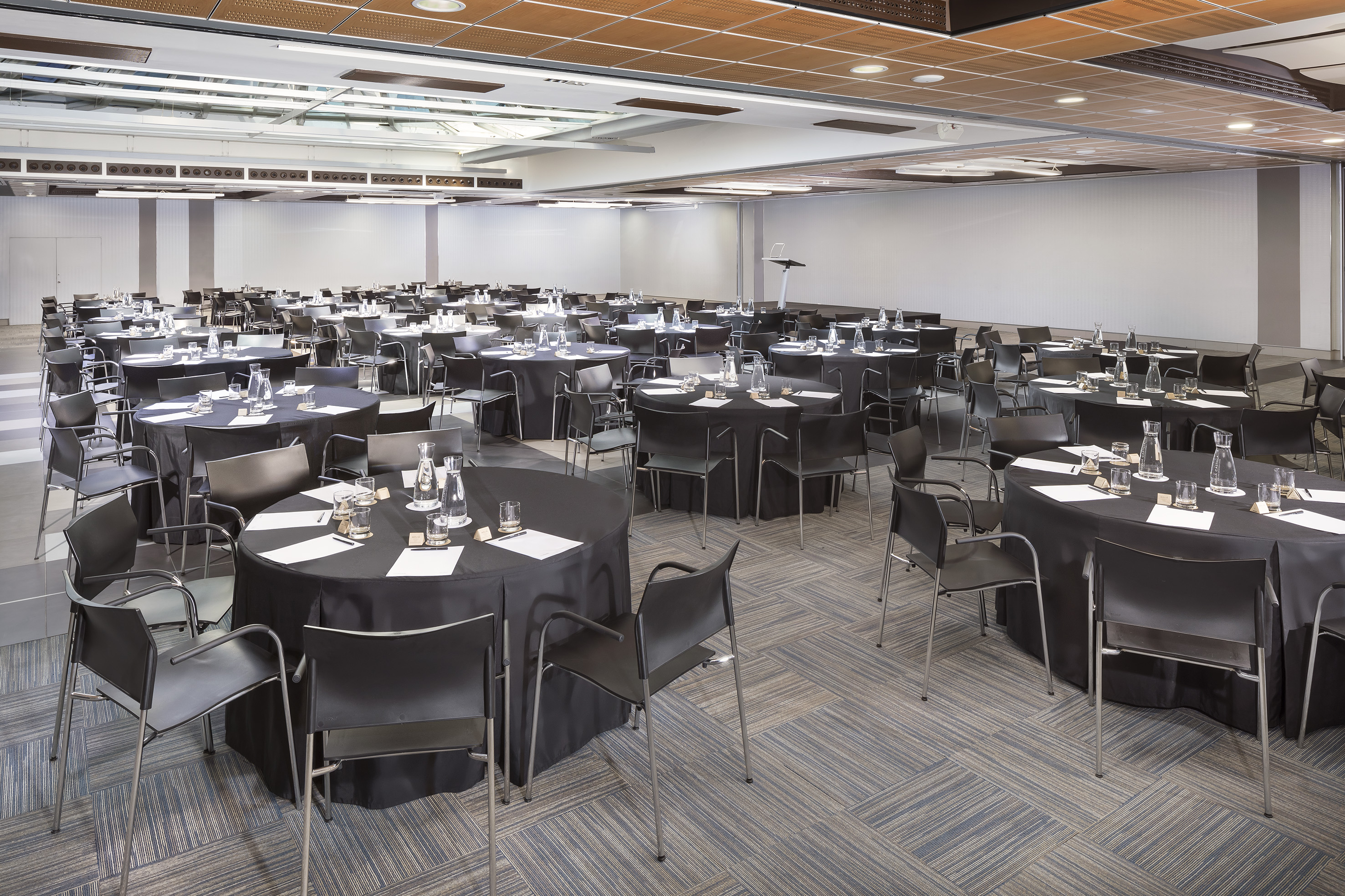 Conference room with black round tables, chairs, and full place settings.
