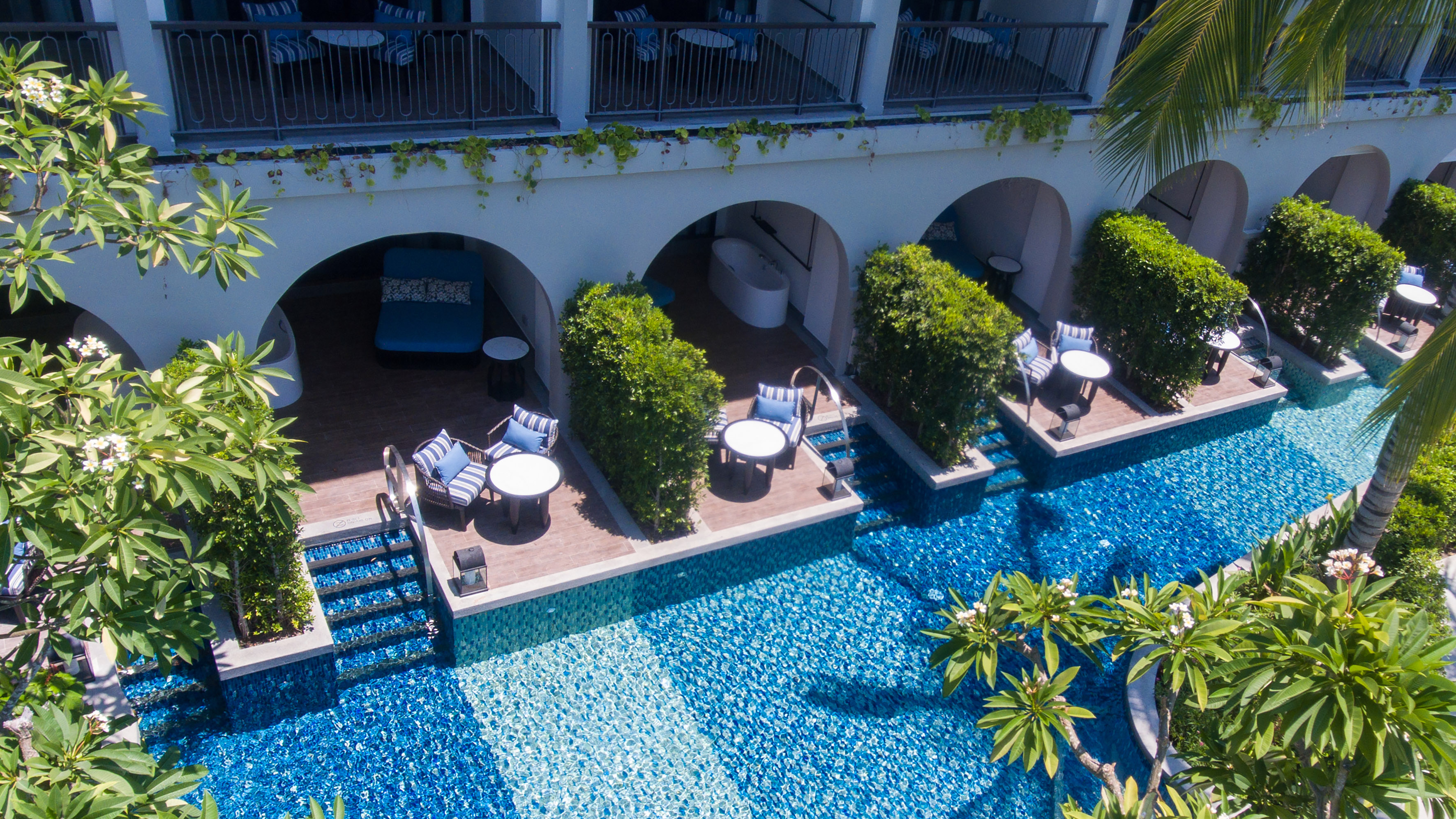 Luxury resort swim-up suites with blue mosaic pool and tropical plants.