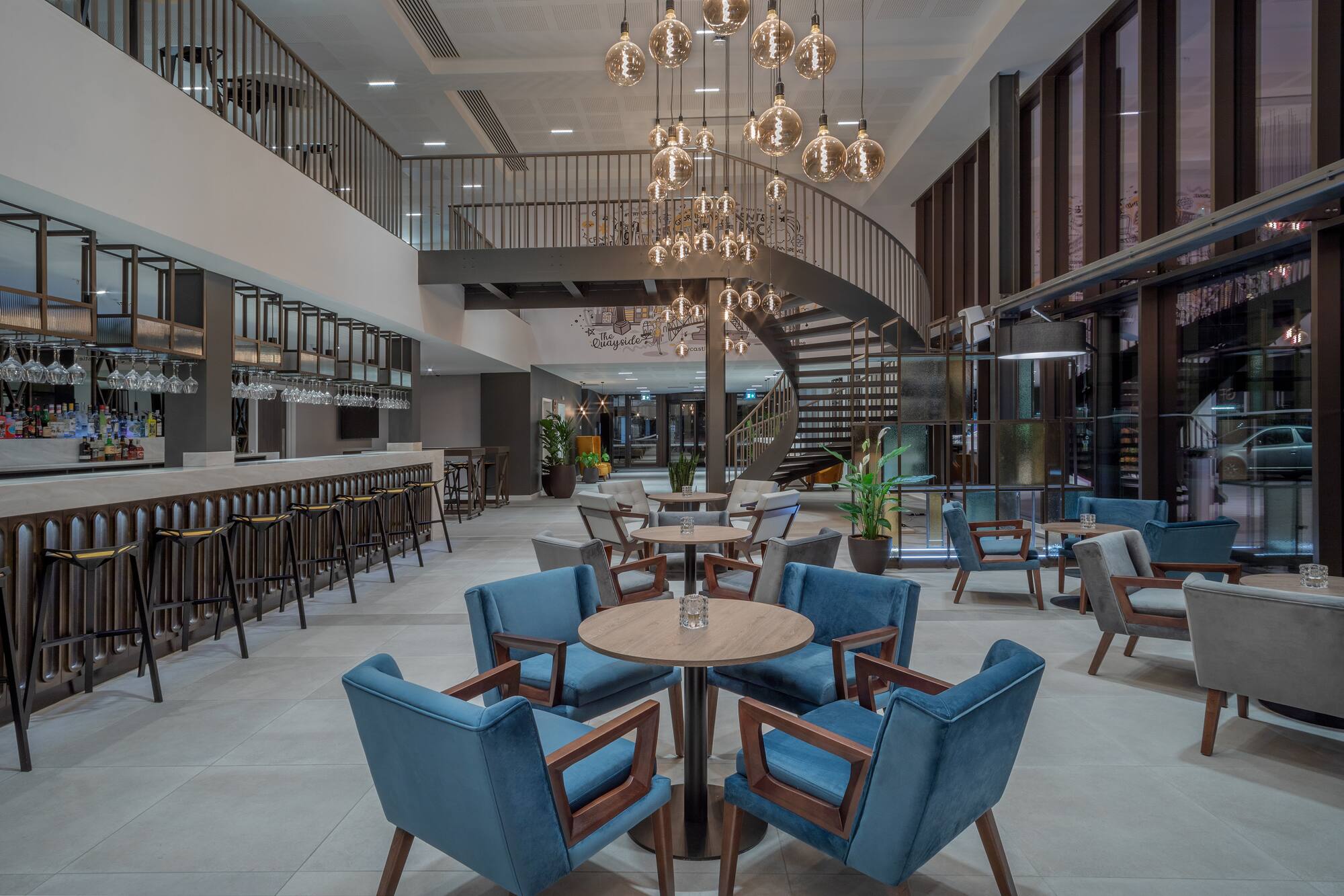 Modern hotel lobby with bar, spiral staircase, and contemporary seating areas.