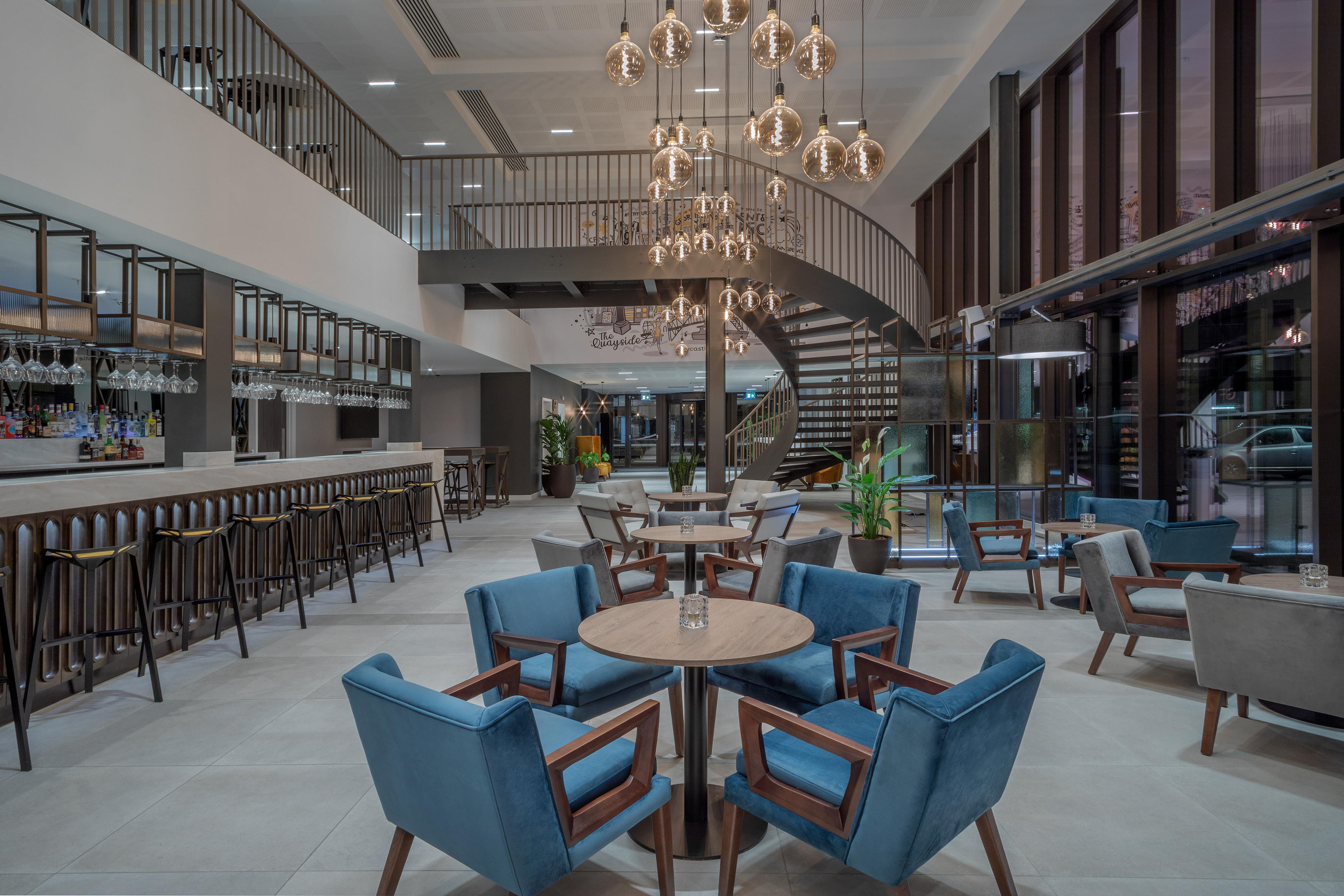 Modern hotel lobby with bar, spiral staircase, and contemporary seating areas.