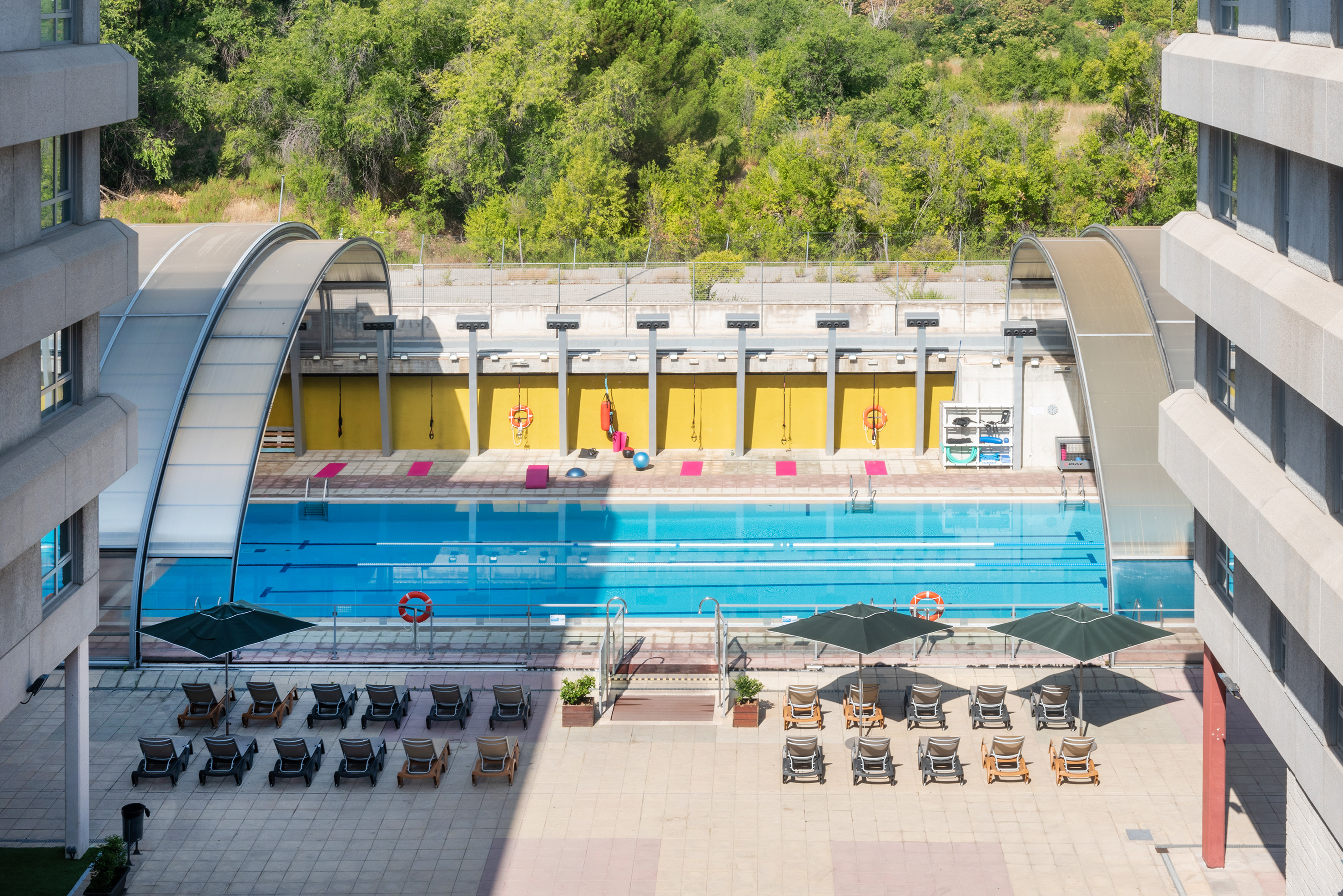 Hotel outdoor pool with loungers, umbrellas, and covered fitness area.
