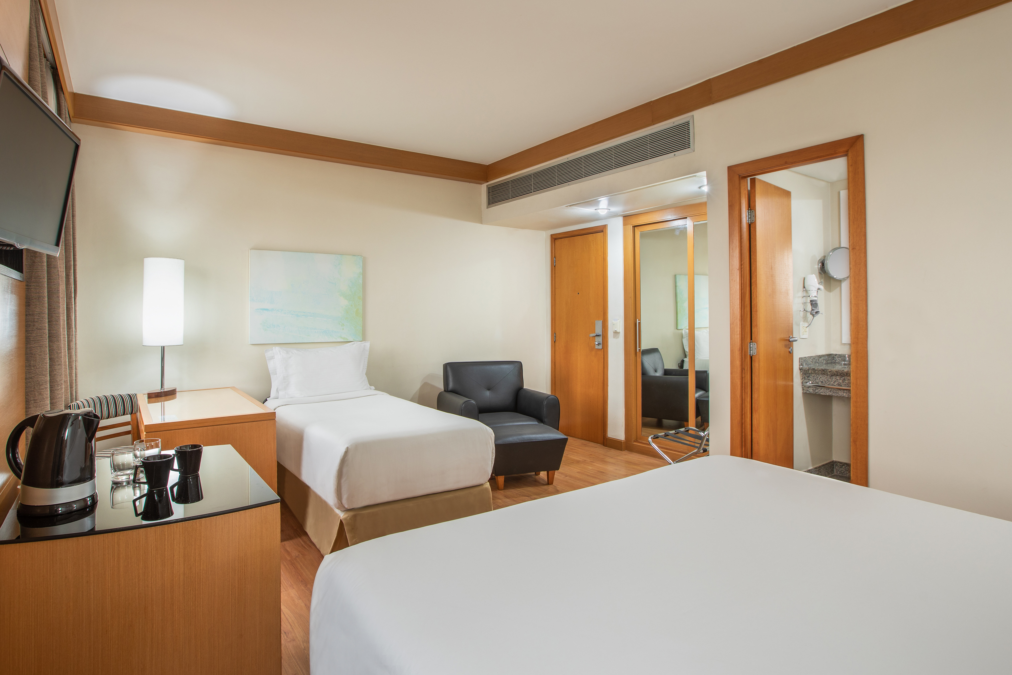 Comfortable hotel guest room with two beds, armchair, and tea station.