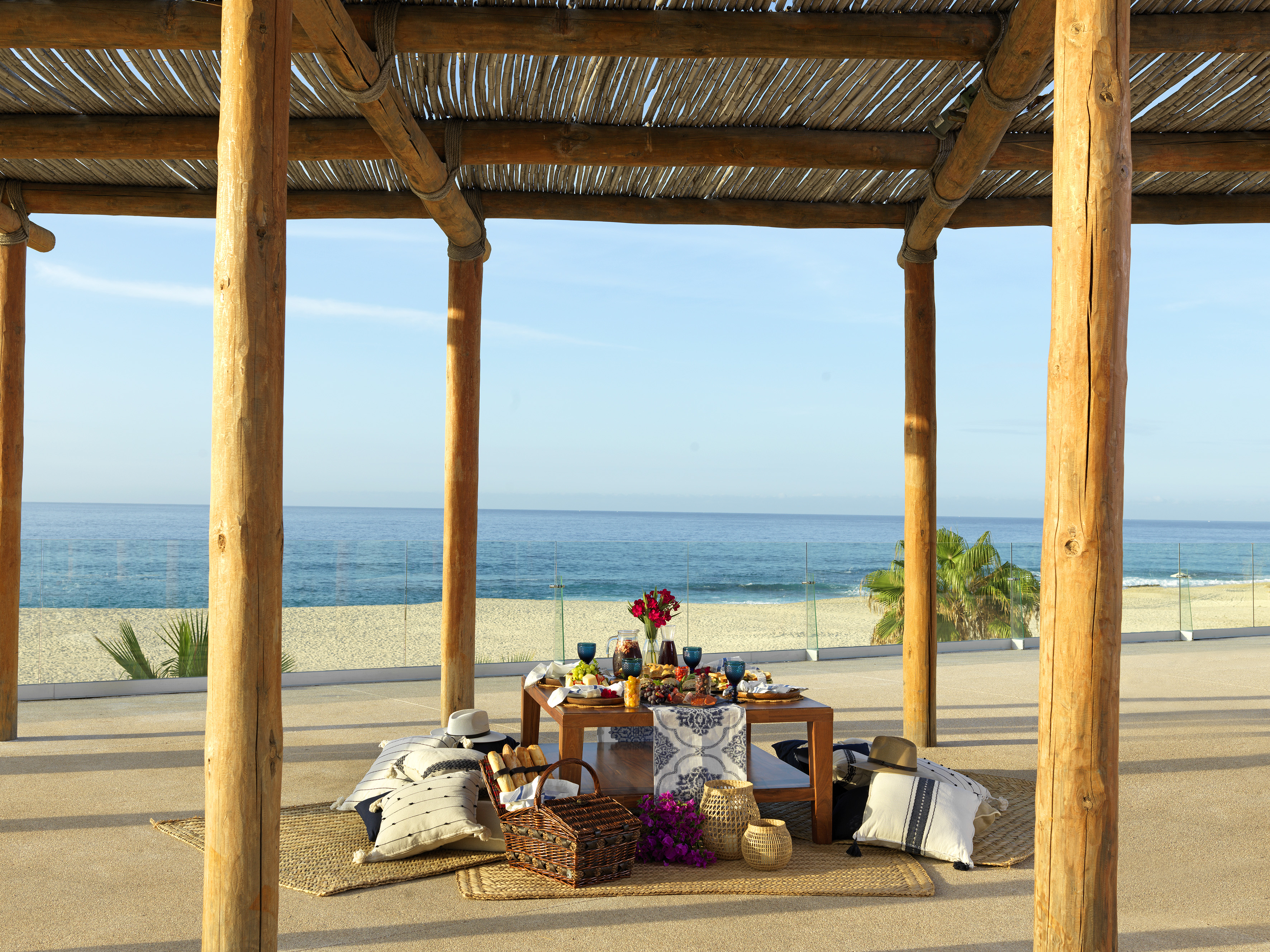Beach picnic setup under rustic pergola with ocean view.