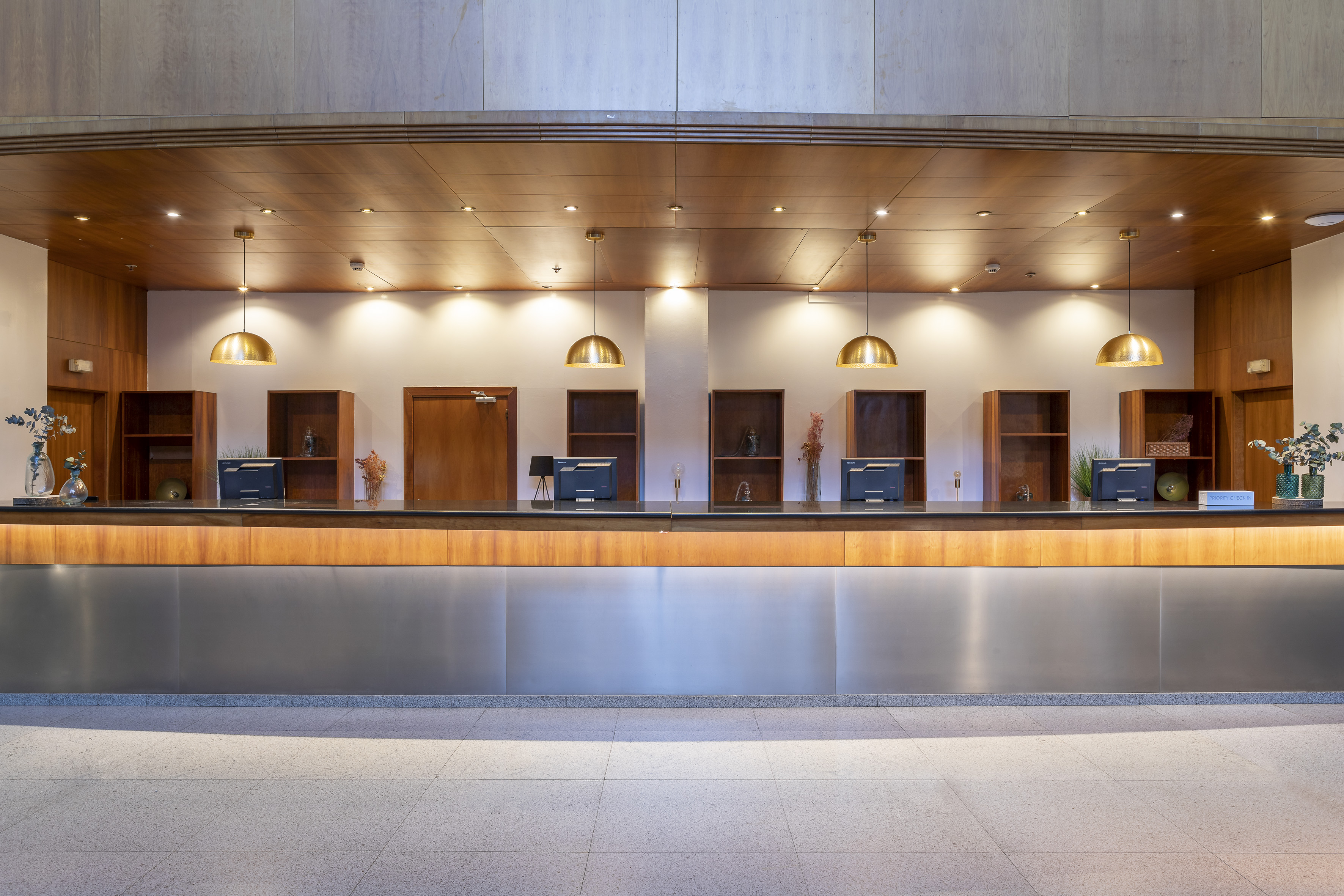 Hotel reception desk featuring wood panels, brass pendant lights, and four monitors.