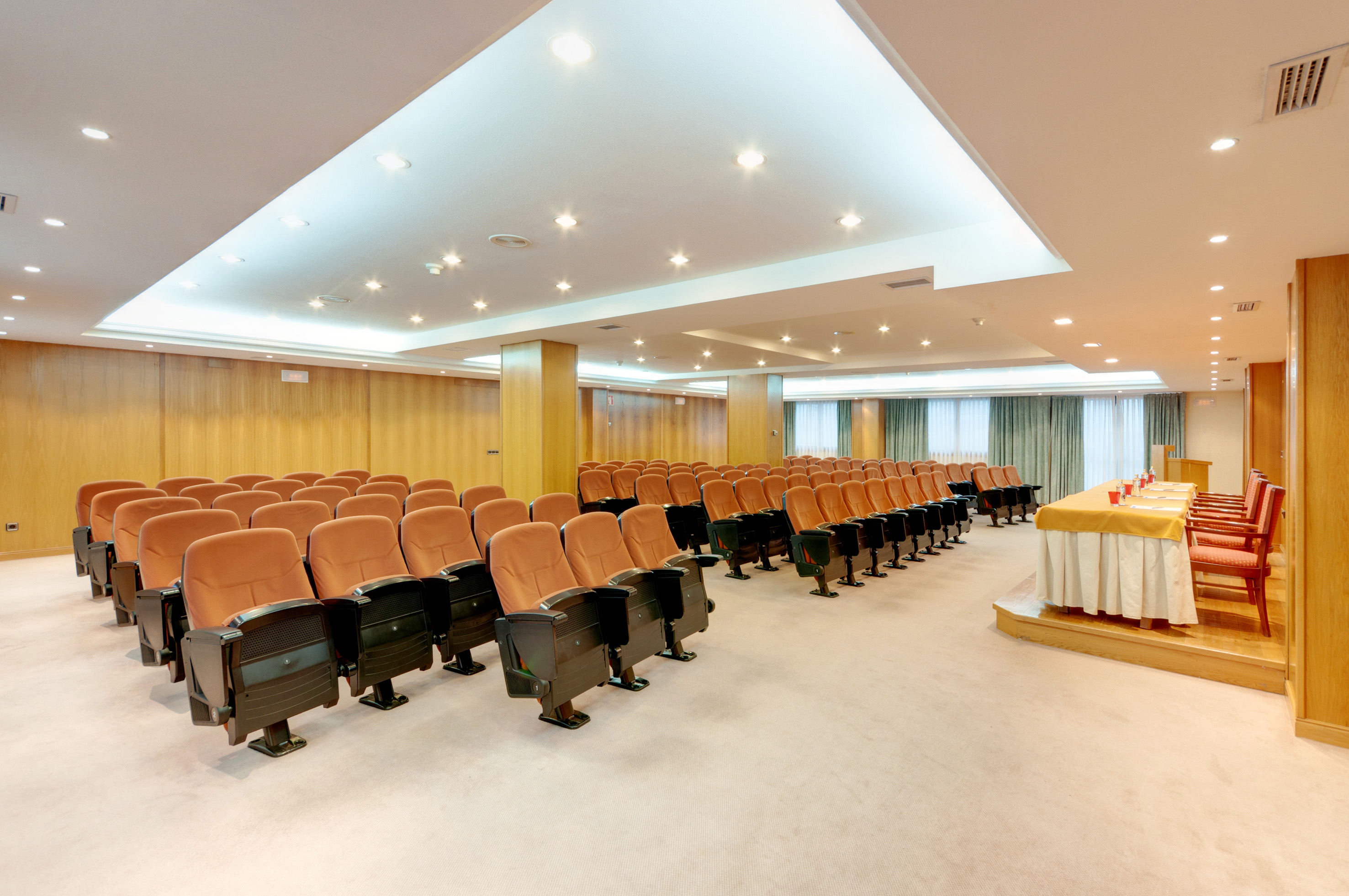 Spacious conference room with empty orange seating, wooden walls, and stage.