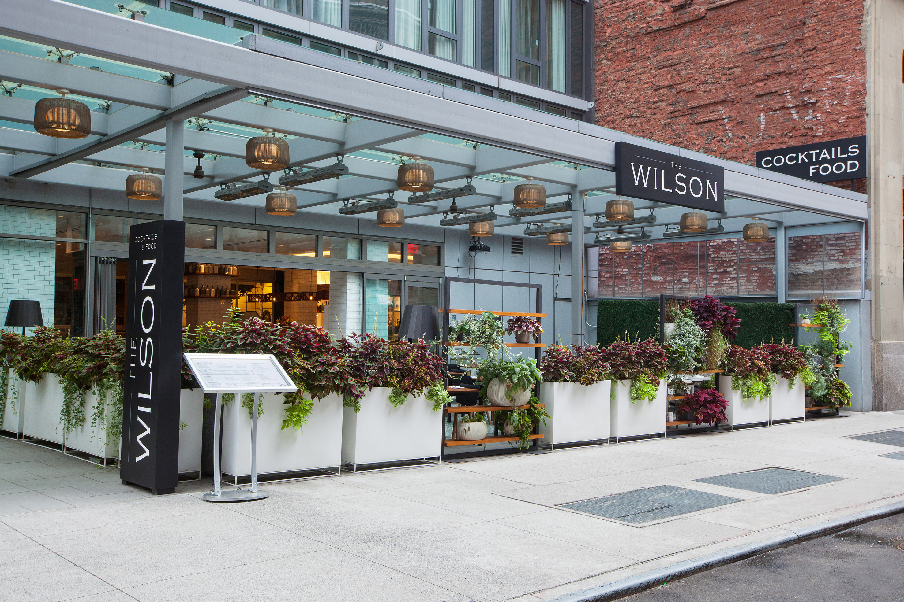 The Wilson restaurant outdoor patio with lush plants and "Cocktails Food" sign.