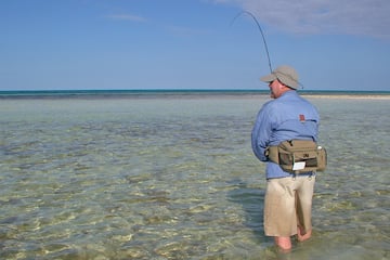 a man standing in shallow water holding a fishing pole