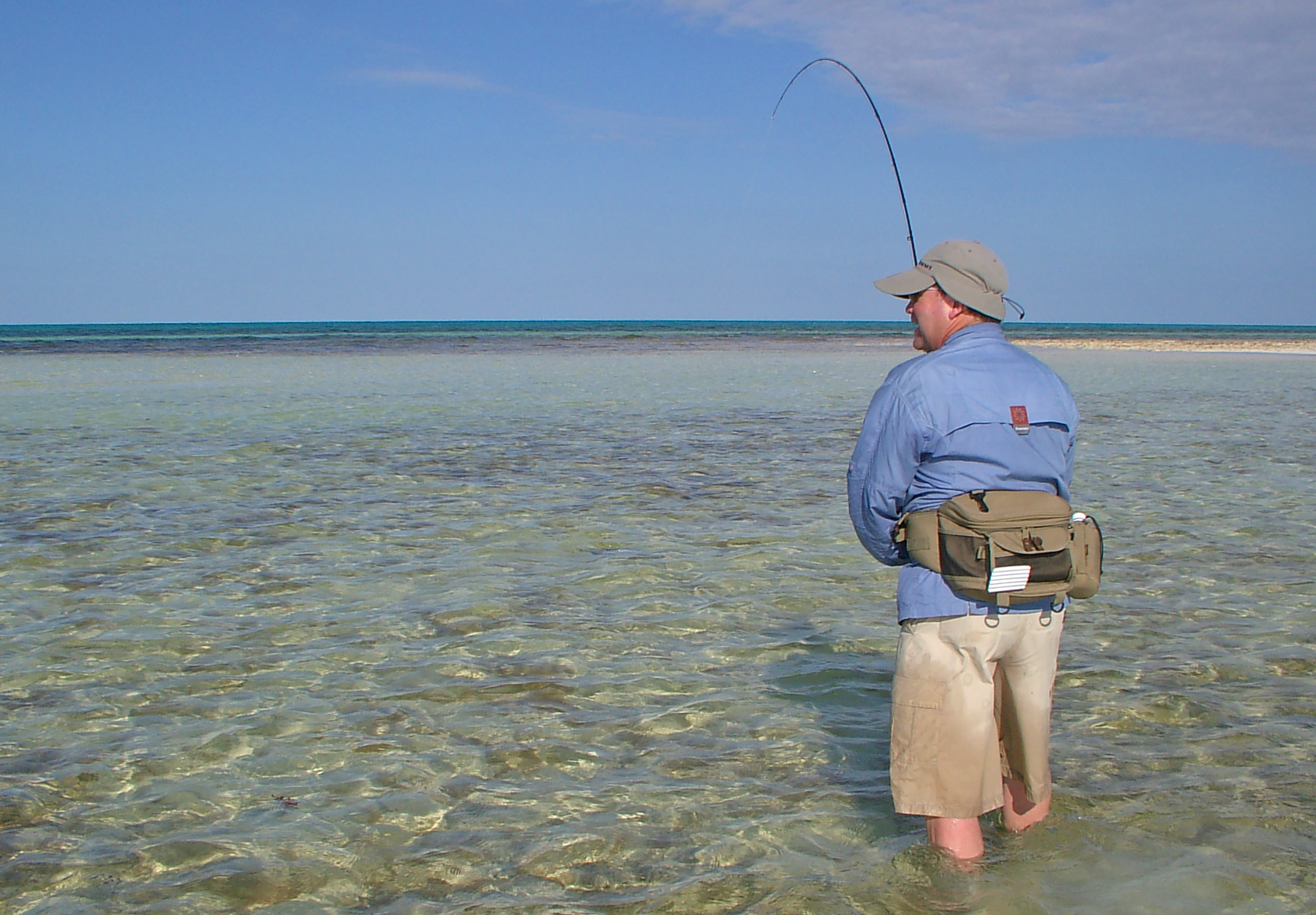 a man standing in shallow water holding a fishing pole