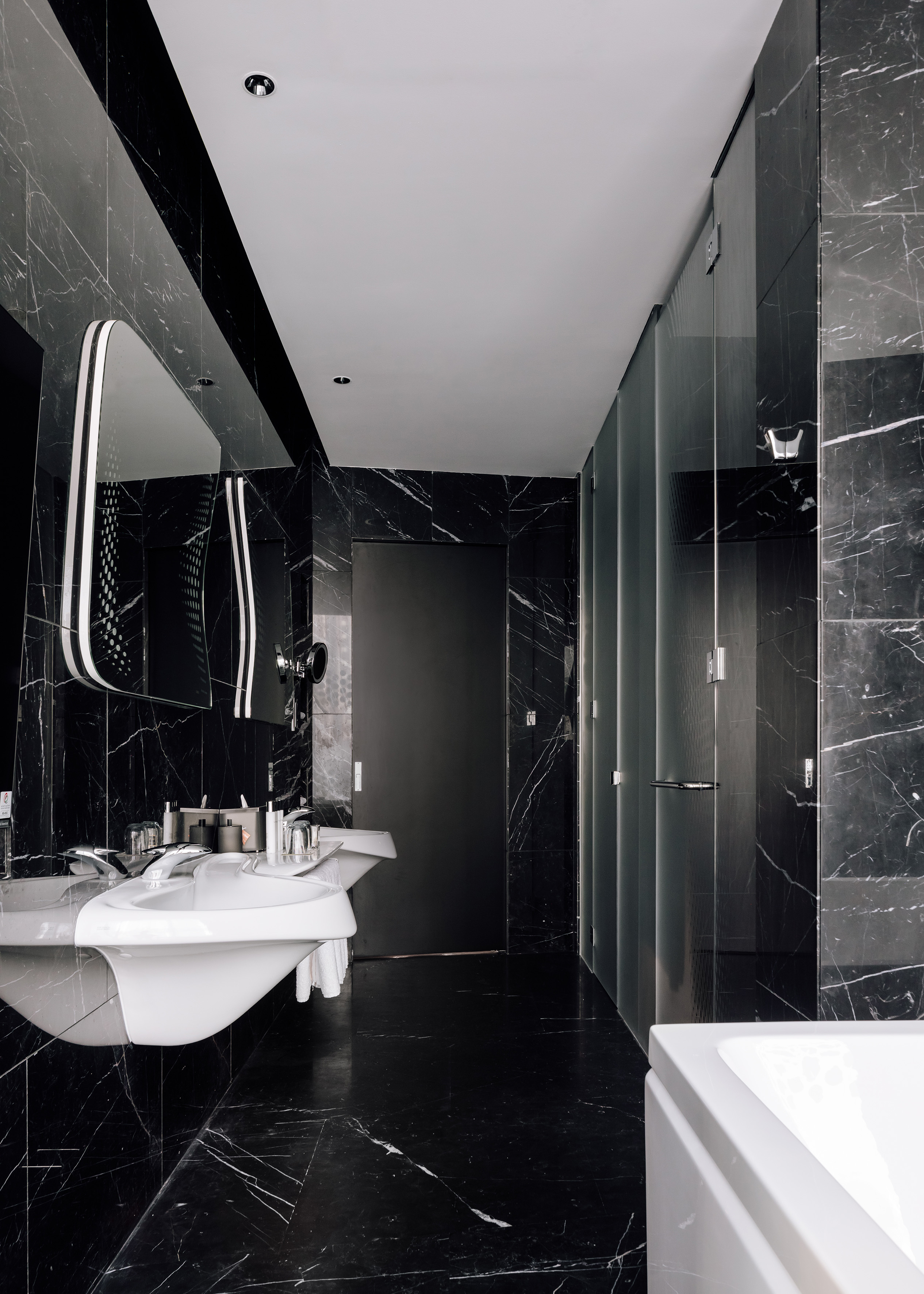 Contemporary black marble bathroom featuring double vanity and glass shower.