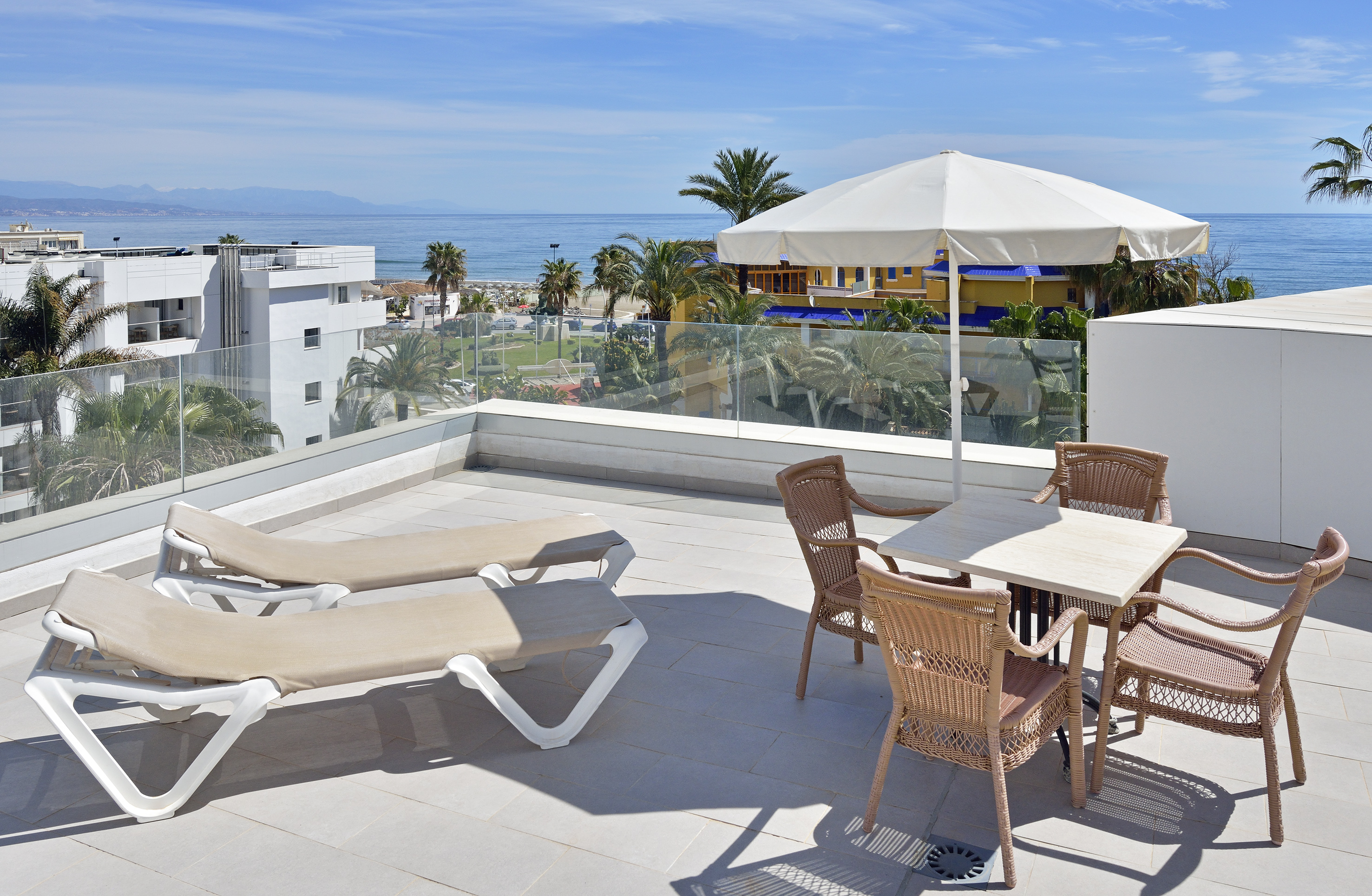 Rooftop terrace with ocean view, sun loungers, dining set, and palm trees.