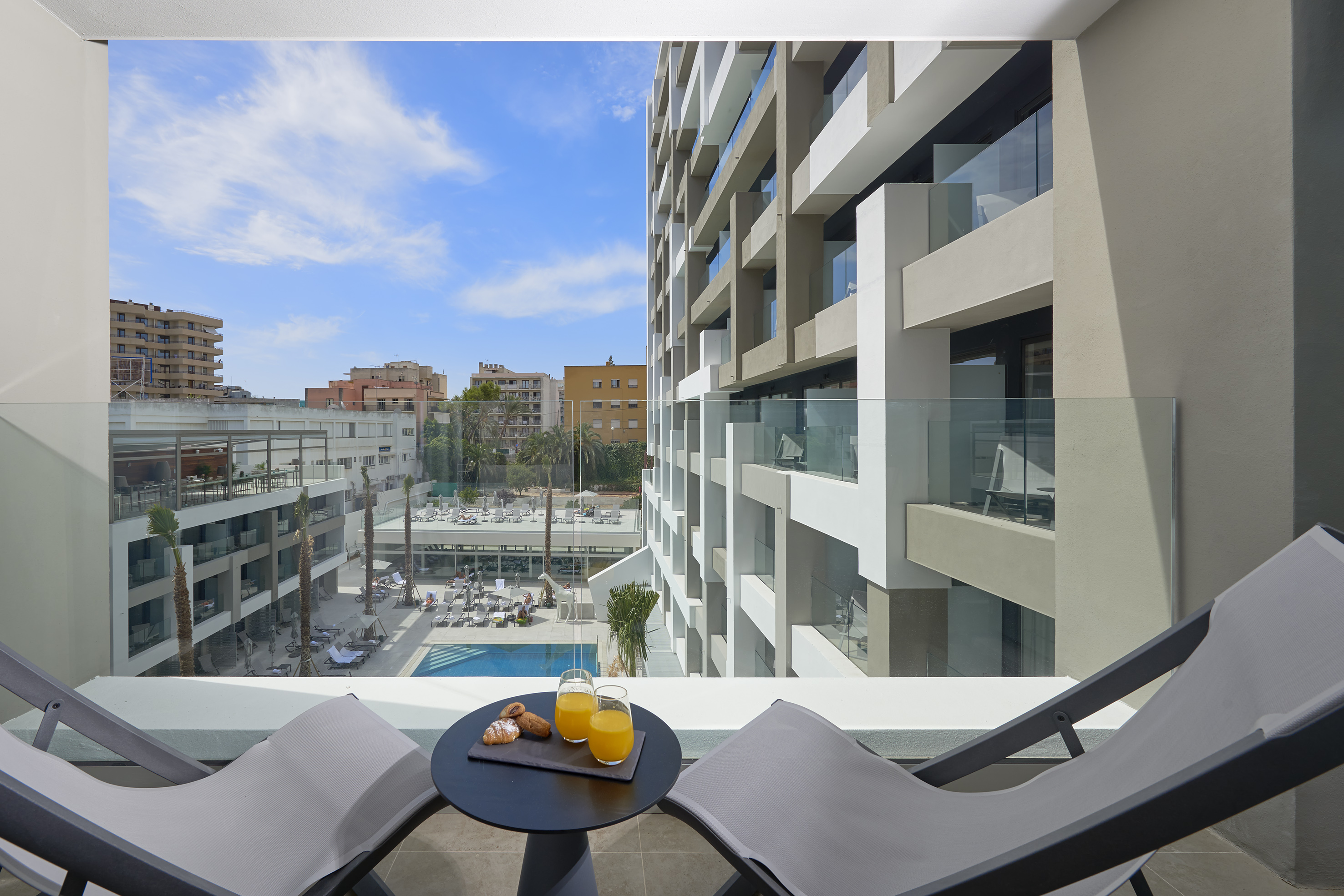 Balcony breakfast with orange juice, lounge chairs, and resort pool view.