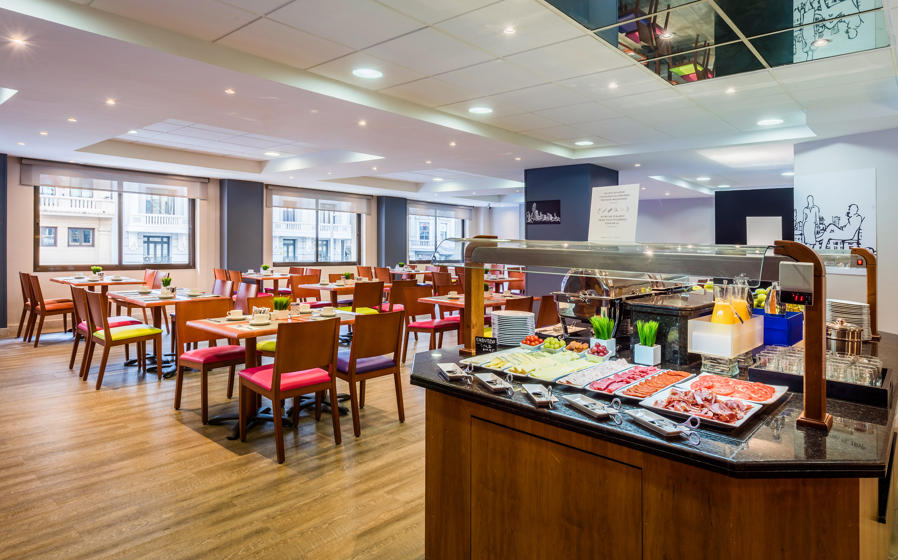 Hotel breakfast buffet with cold cuts, juices, and a vibrant dining area.