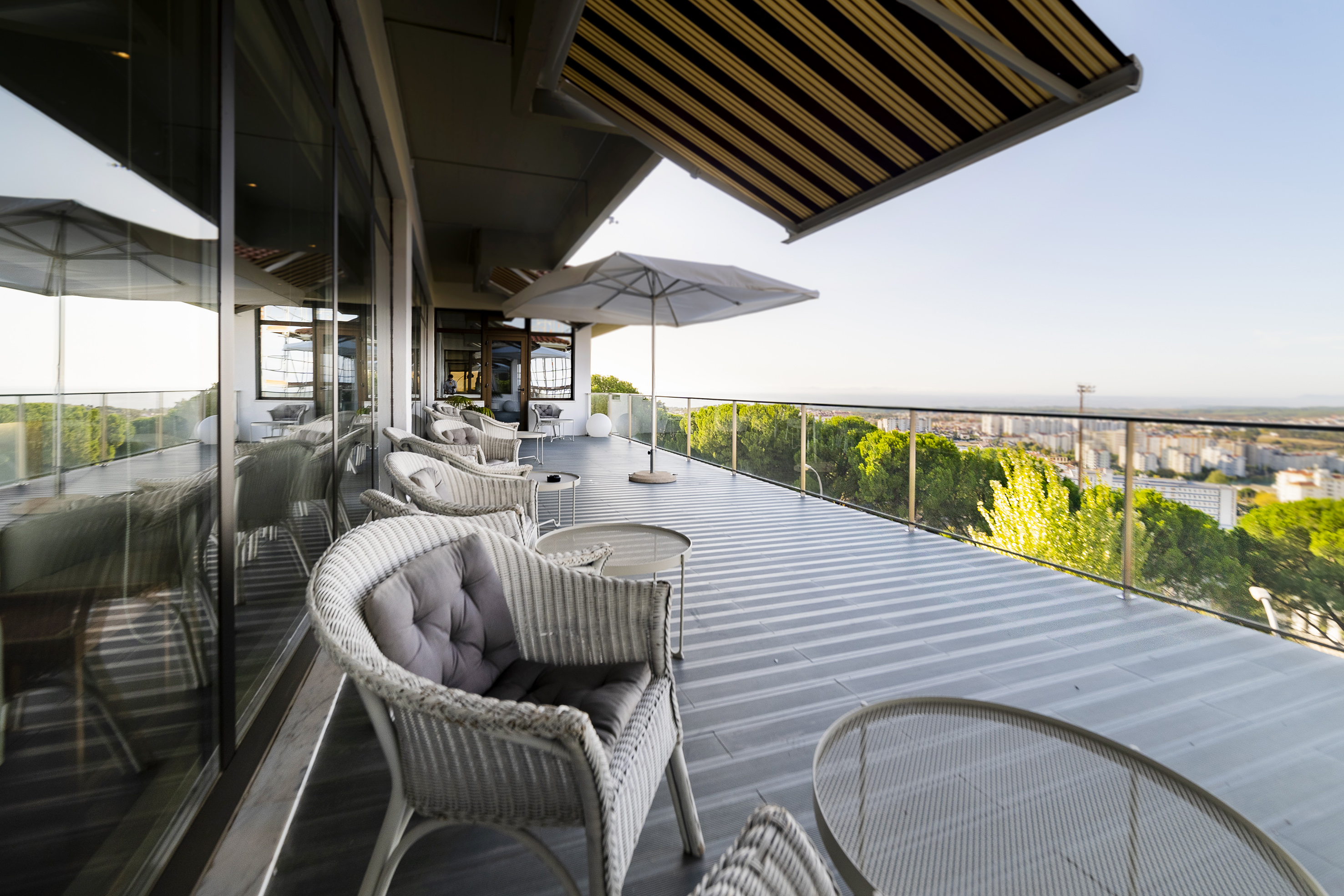 Outdoor lounge balcony with modern wicker furniture and city panorama.