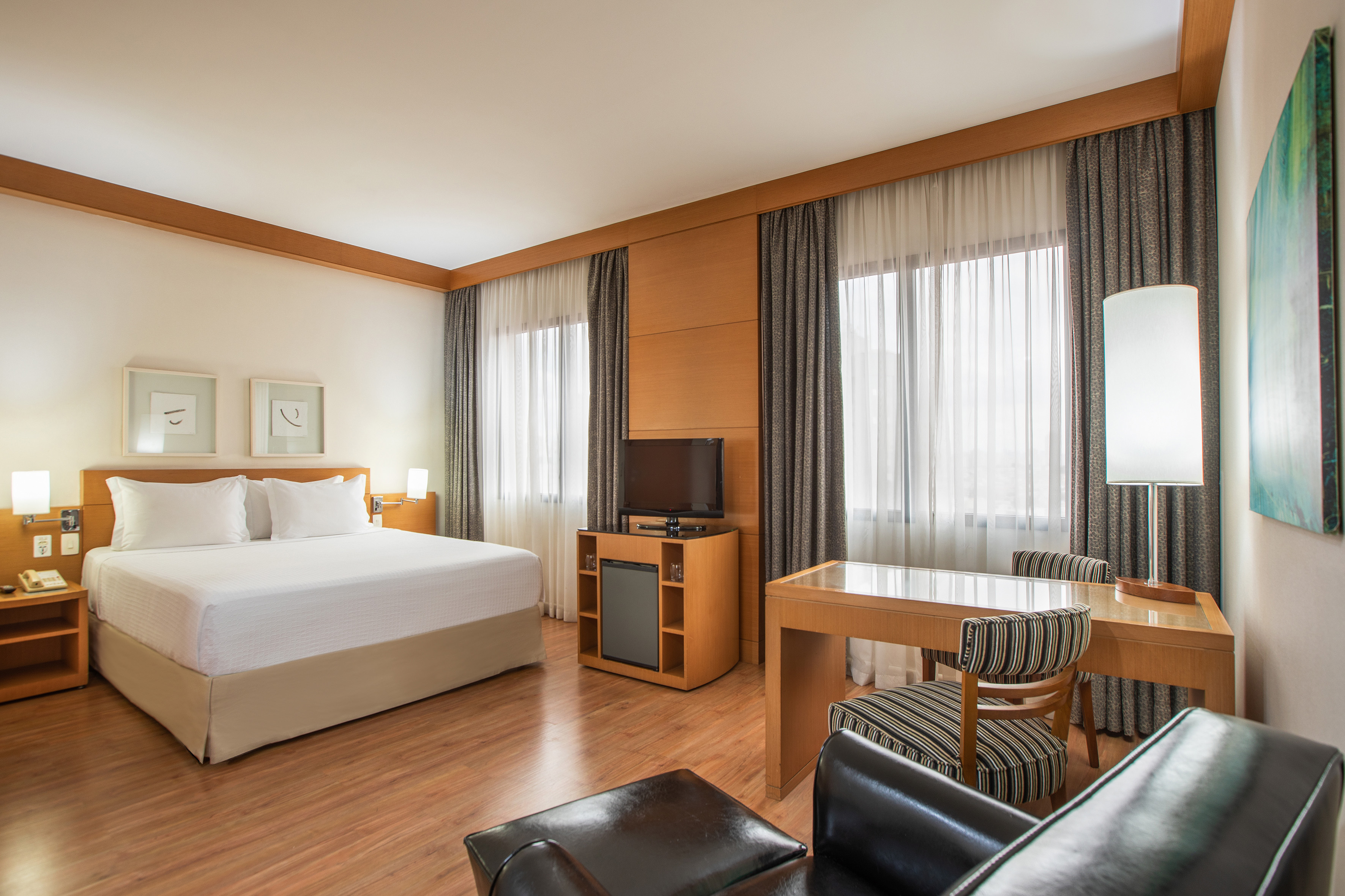 Spacious hotel room with king bed, work desk, TV, and modern decor.