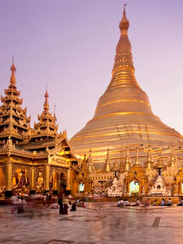 a large gold building with a pointed top with Shwedagon Pagoda in the background