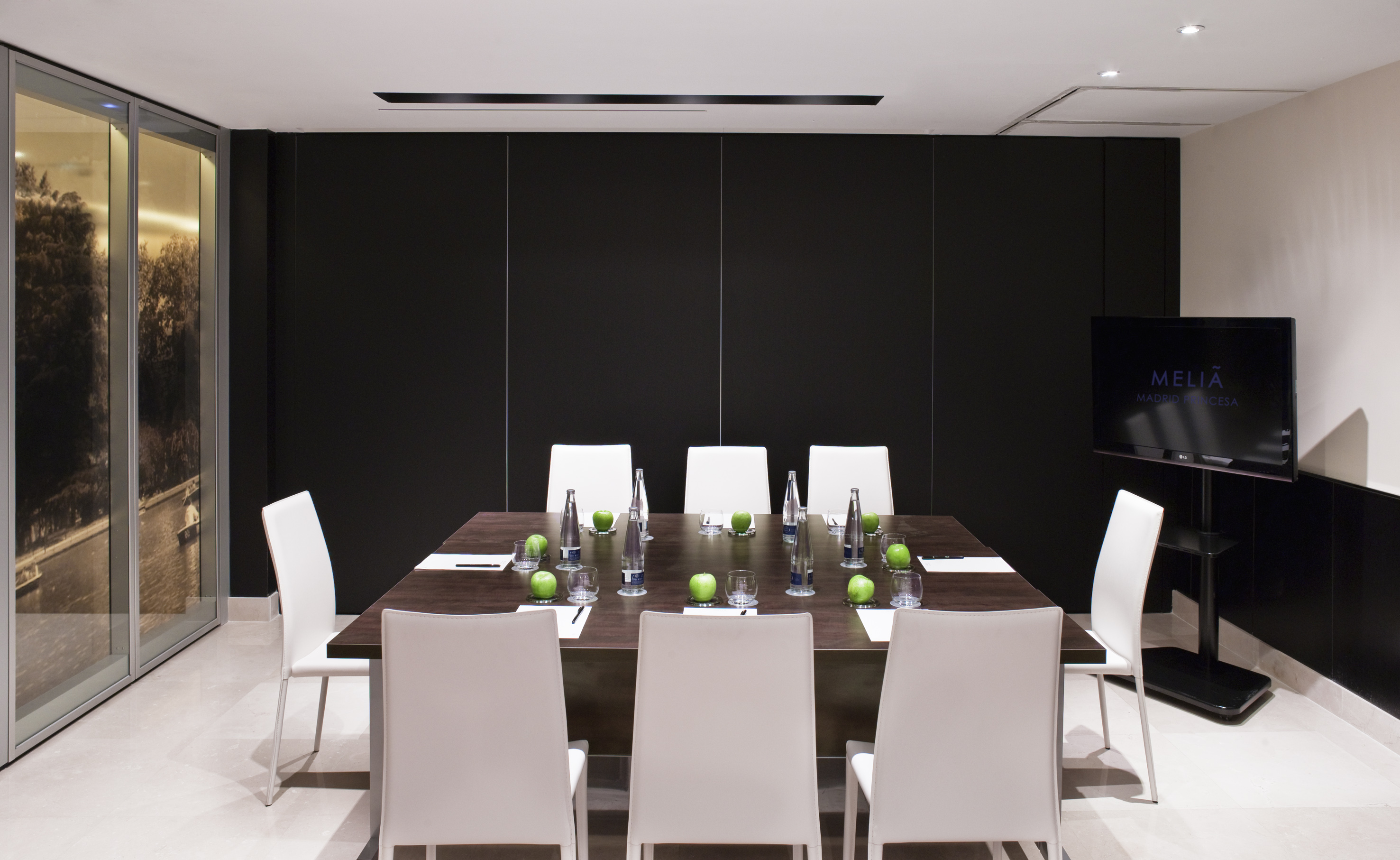 Modern Meliá hotel meeting room with dark table, white chairs, and TV screen.