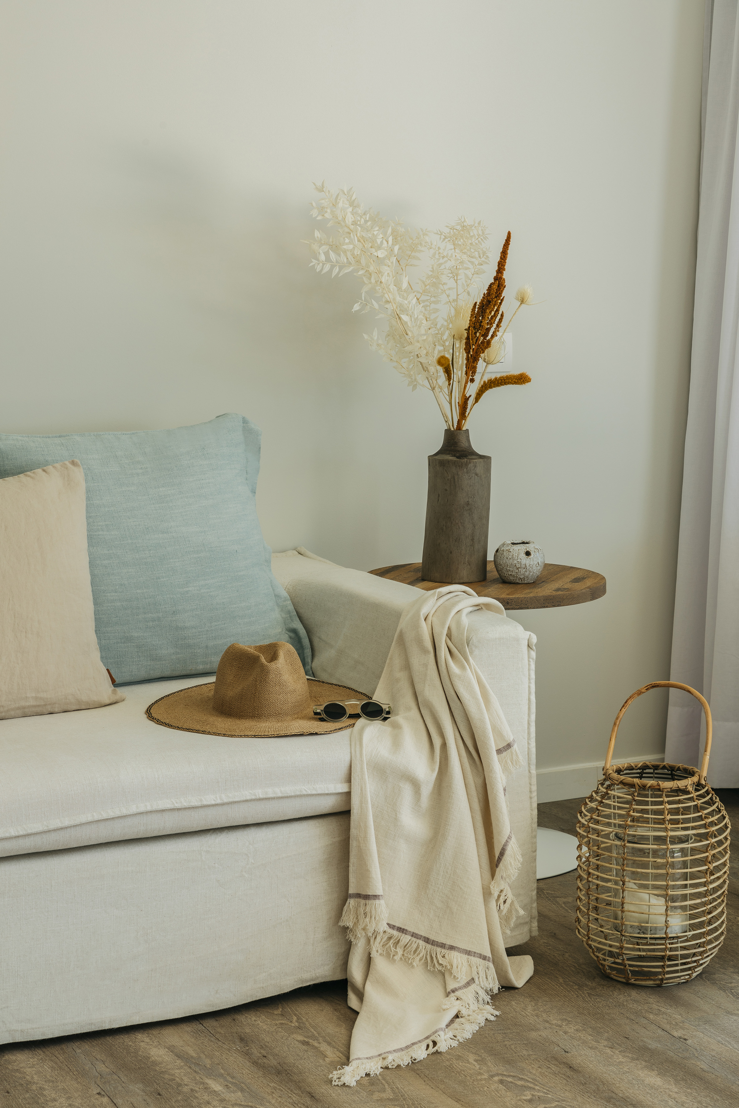 Beige sofa with straw hat, dried flowers, and wicker lantern in natural decor.