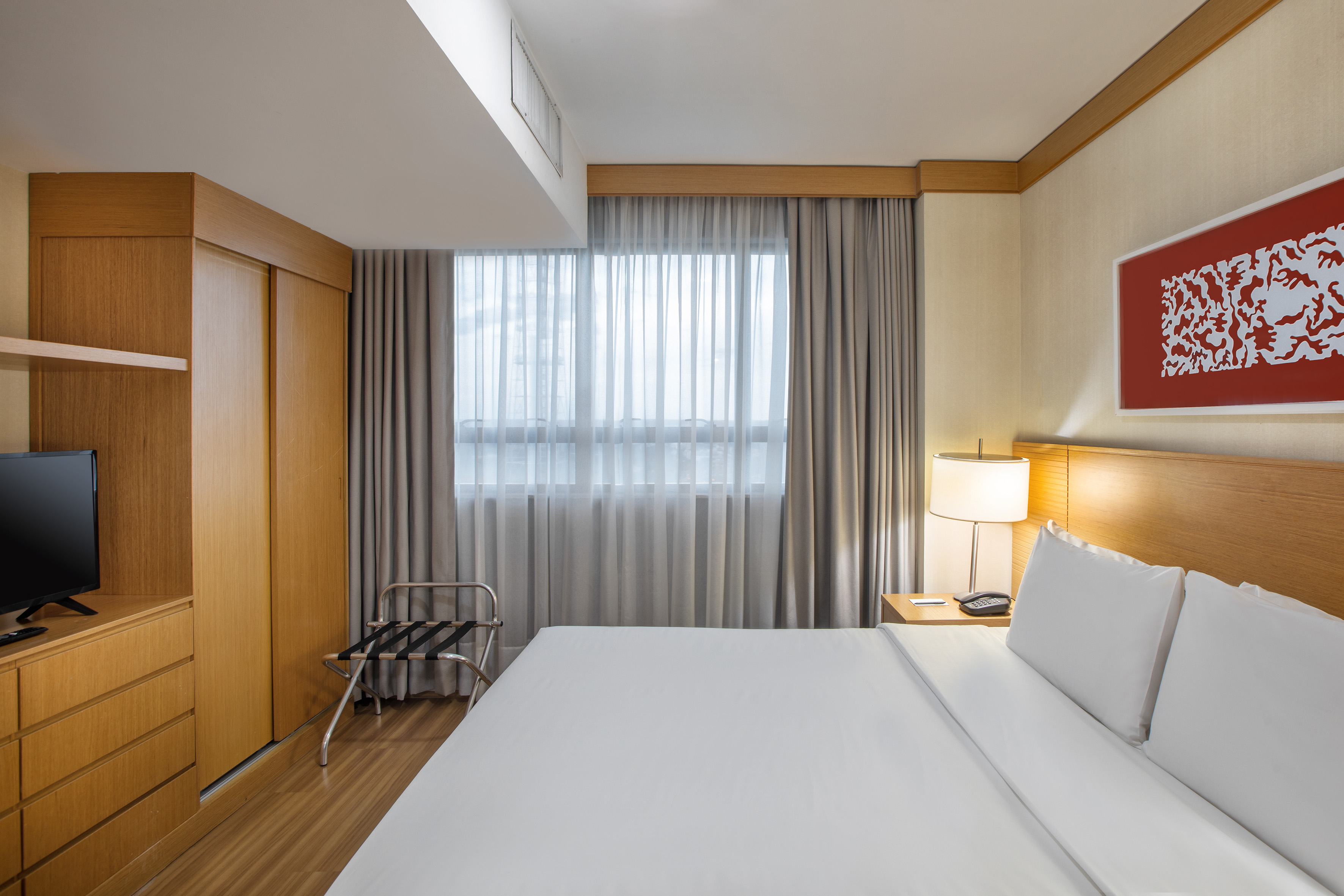 Modern hotel bedroom with large bed, wooden furniture, TV, and window.