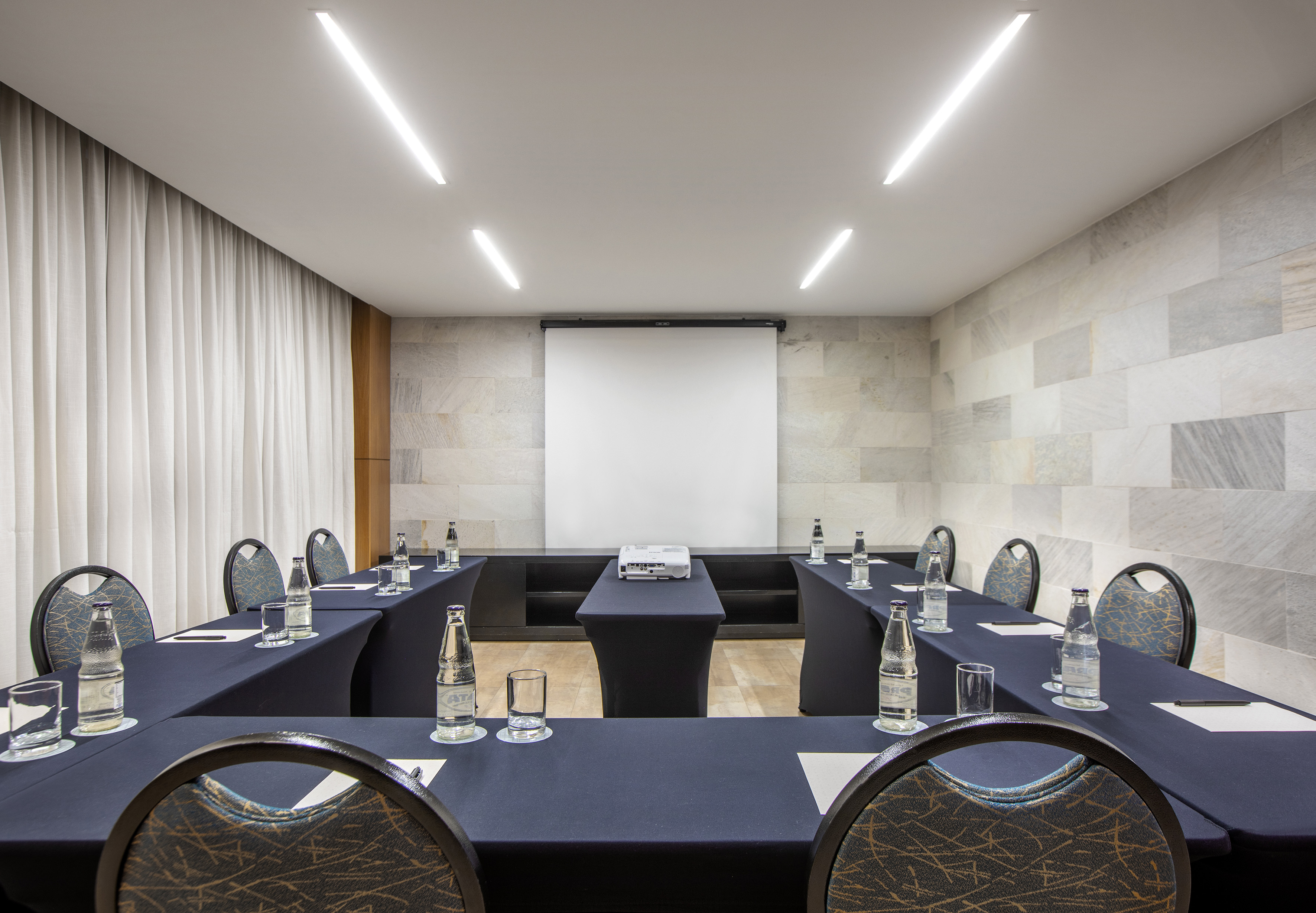 U-shaped conference room with projector screen and bottled water.