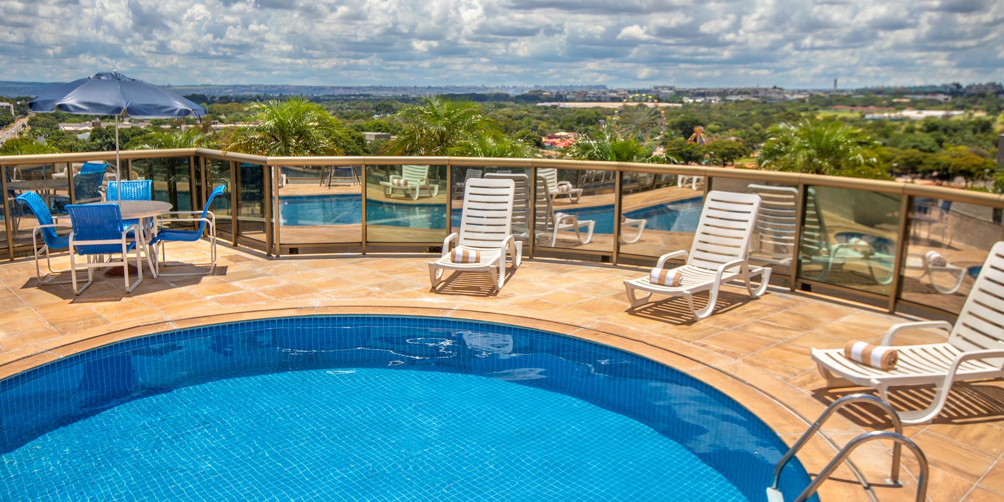 Hotel rooftop pool with lounge chairs, blue umbrella, and city view.