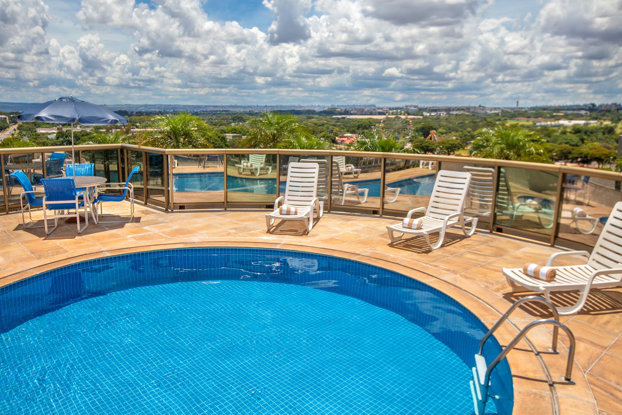 Hotel rooftop pool with lounge chairs, blue umbrella, and city view.