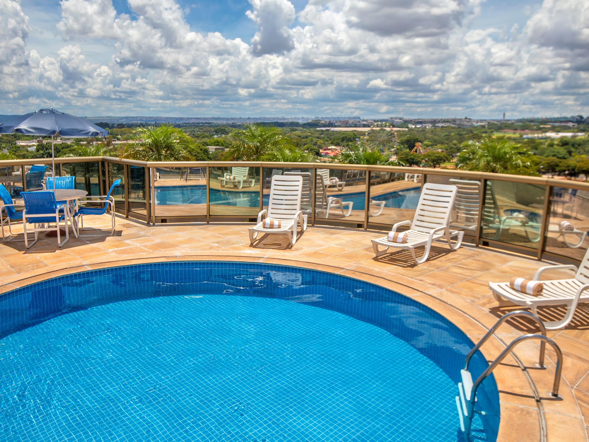 Rooftop swimming pool deck with lounge chairs, blue umbrella, and city view.