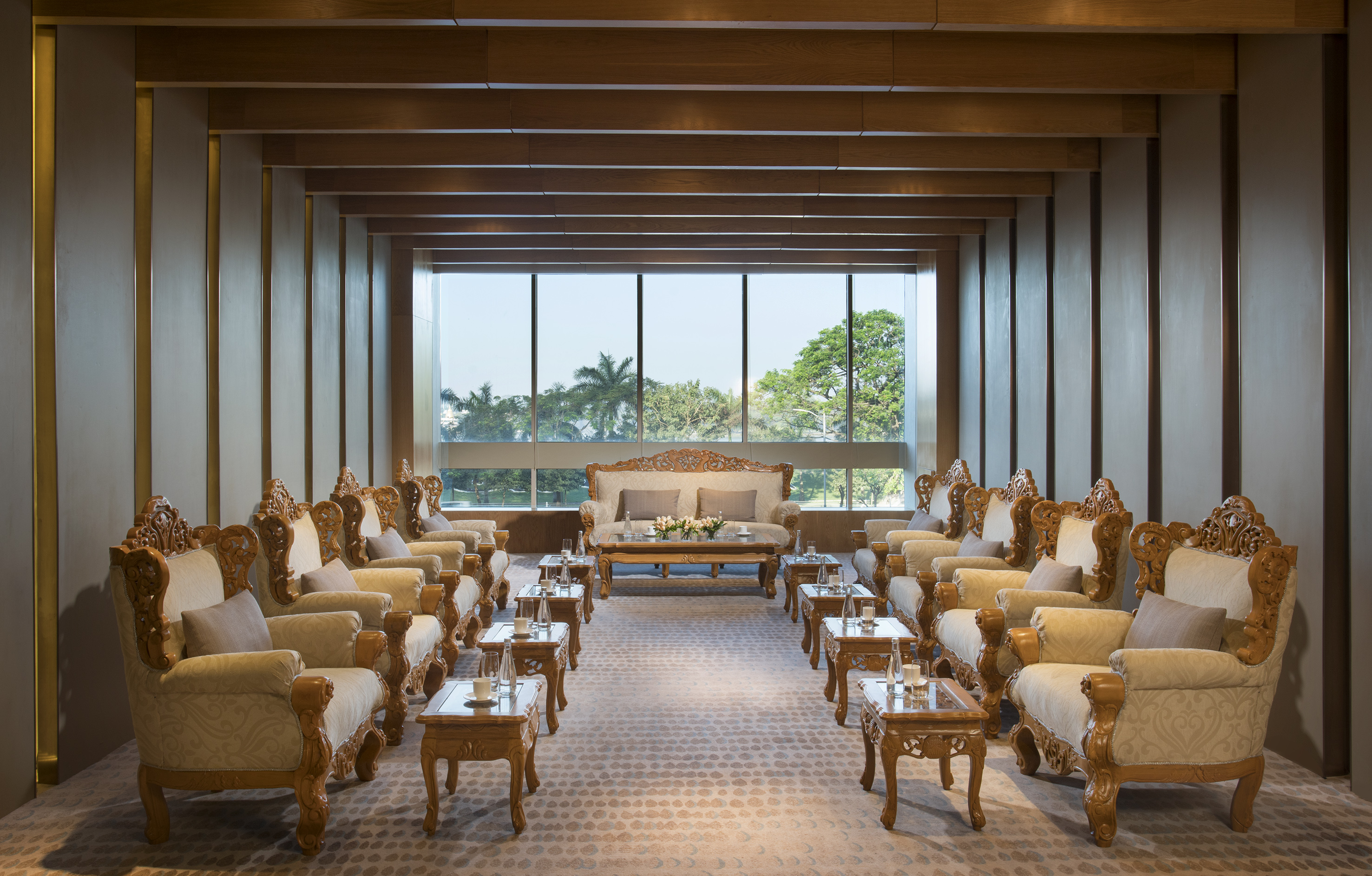 Elegant lounge with ornate chairs, sofa, wooden tables, and scenic window view.