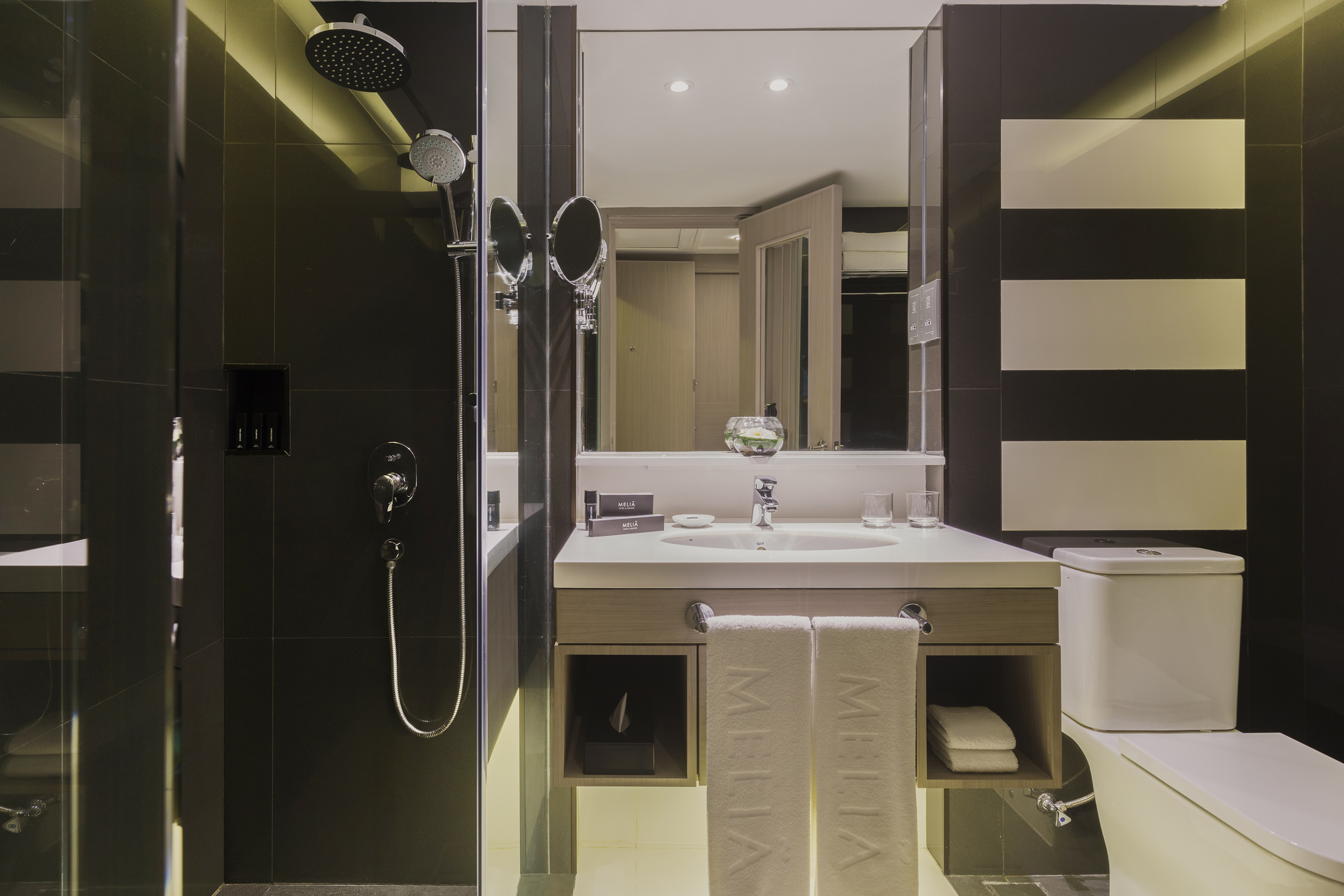 Modern Meliã hotel bathroom with black tiled shower, white vanity, sink, and toilet.
