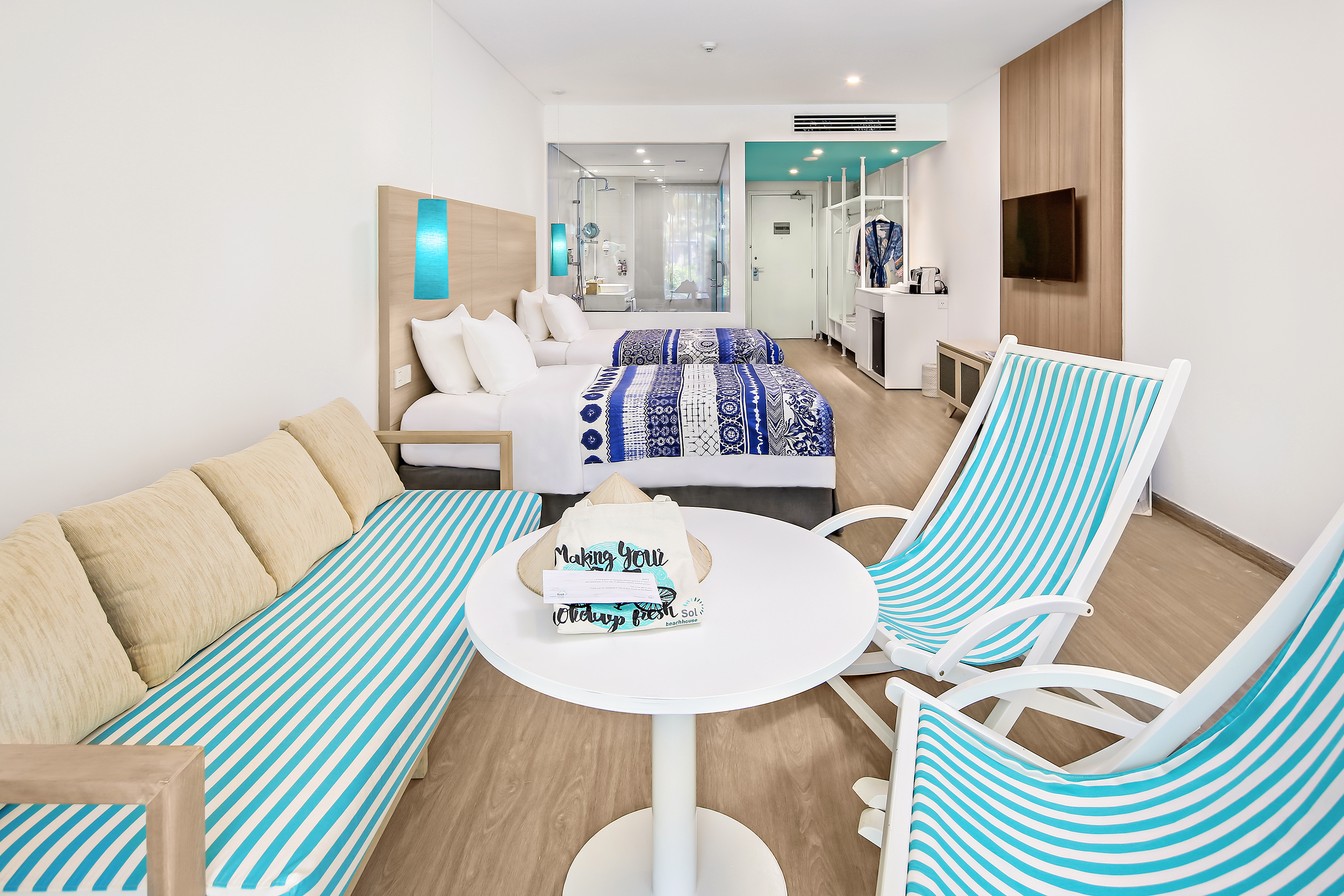 Tropical resort room with two beds, blue striped sofa, and lounge chairs.