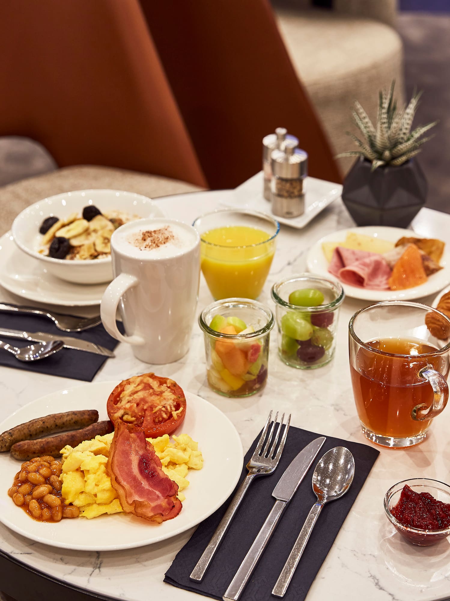 Hotel breakfast with eggs, bacon, pastries, coffee, juice, and fruit salad on a marble table.