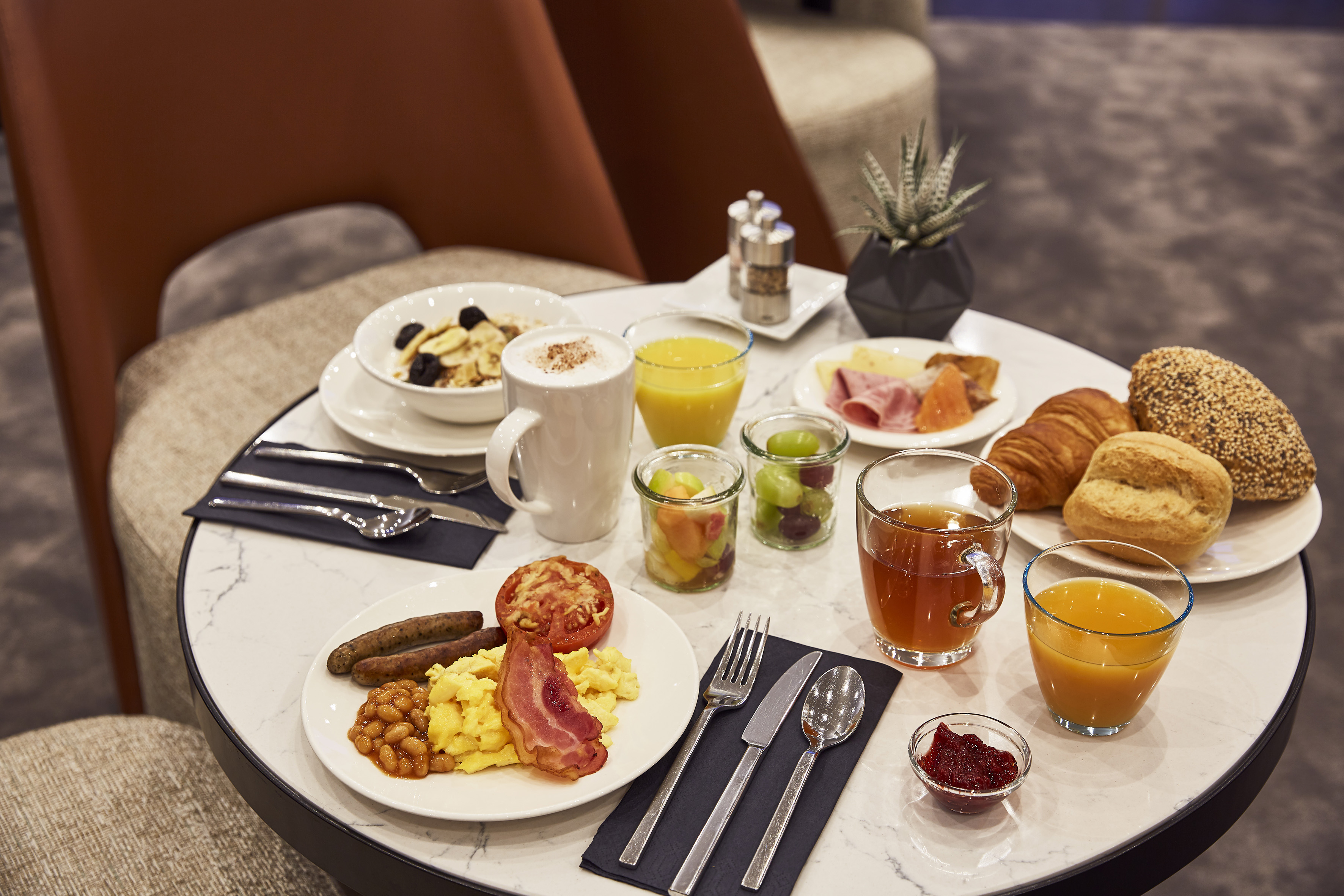 Hotel breakfast with eggs, bacon, pastries, coffee, juice, and fruit salad on a marble table.