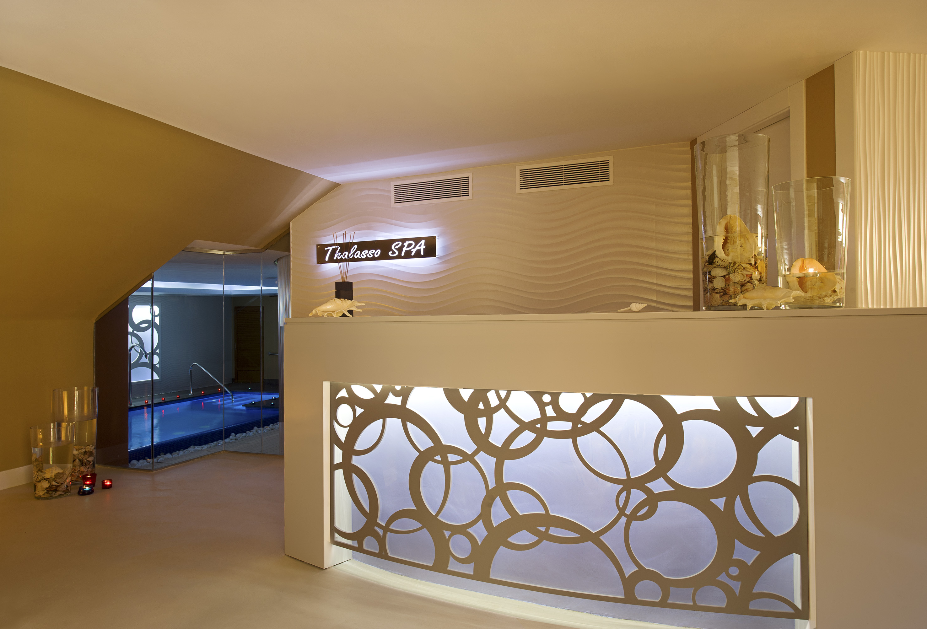 Thalasso SPA reception desk with illuminated design, wavy wall, and indoor pool.