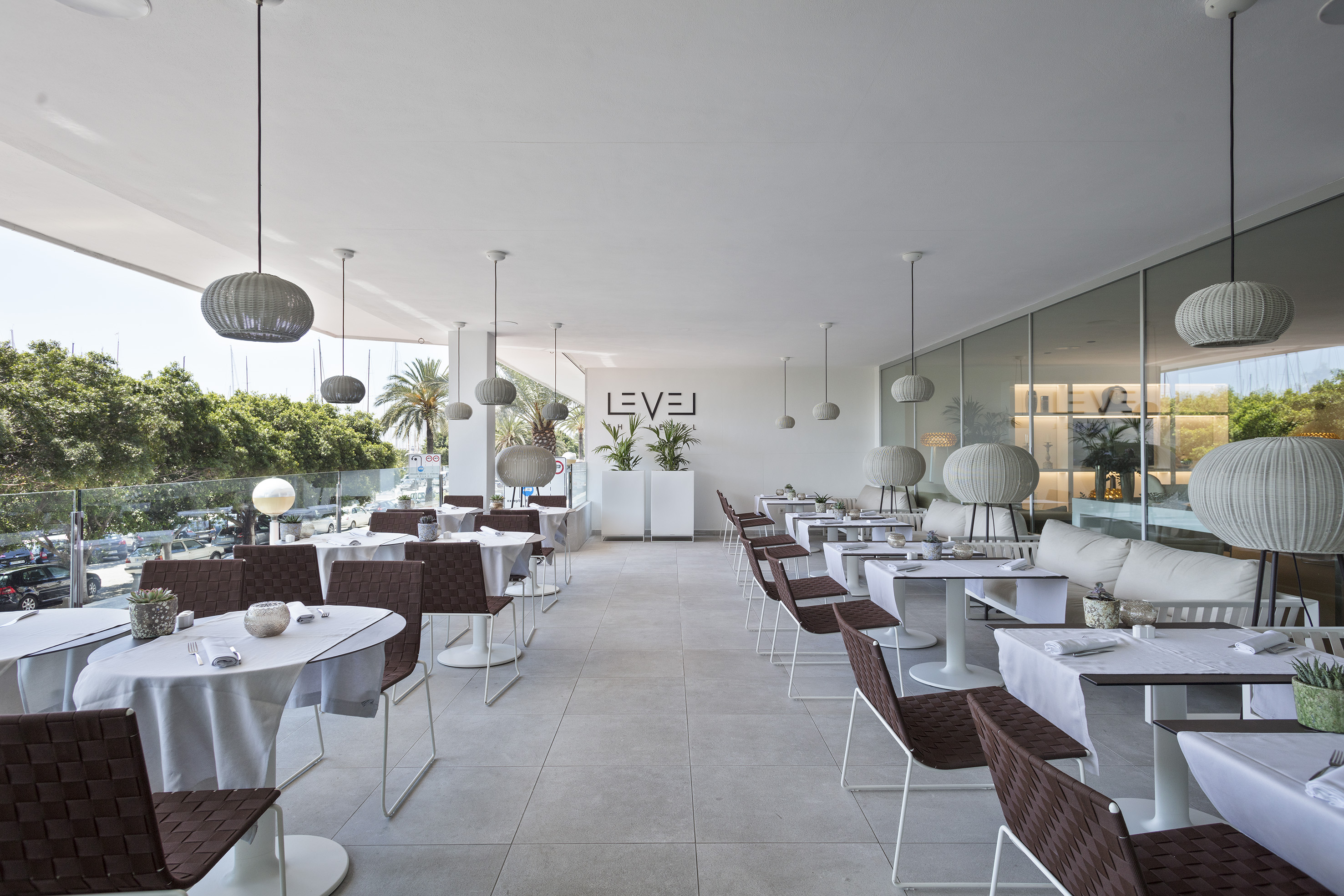 Stylish restaurant patio with white tables, woven chairs, and garden views.