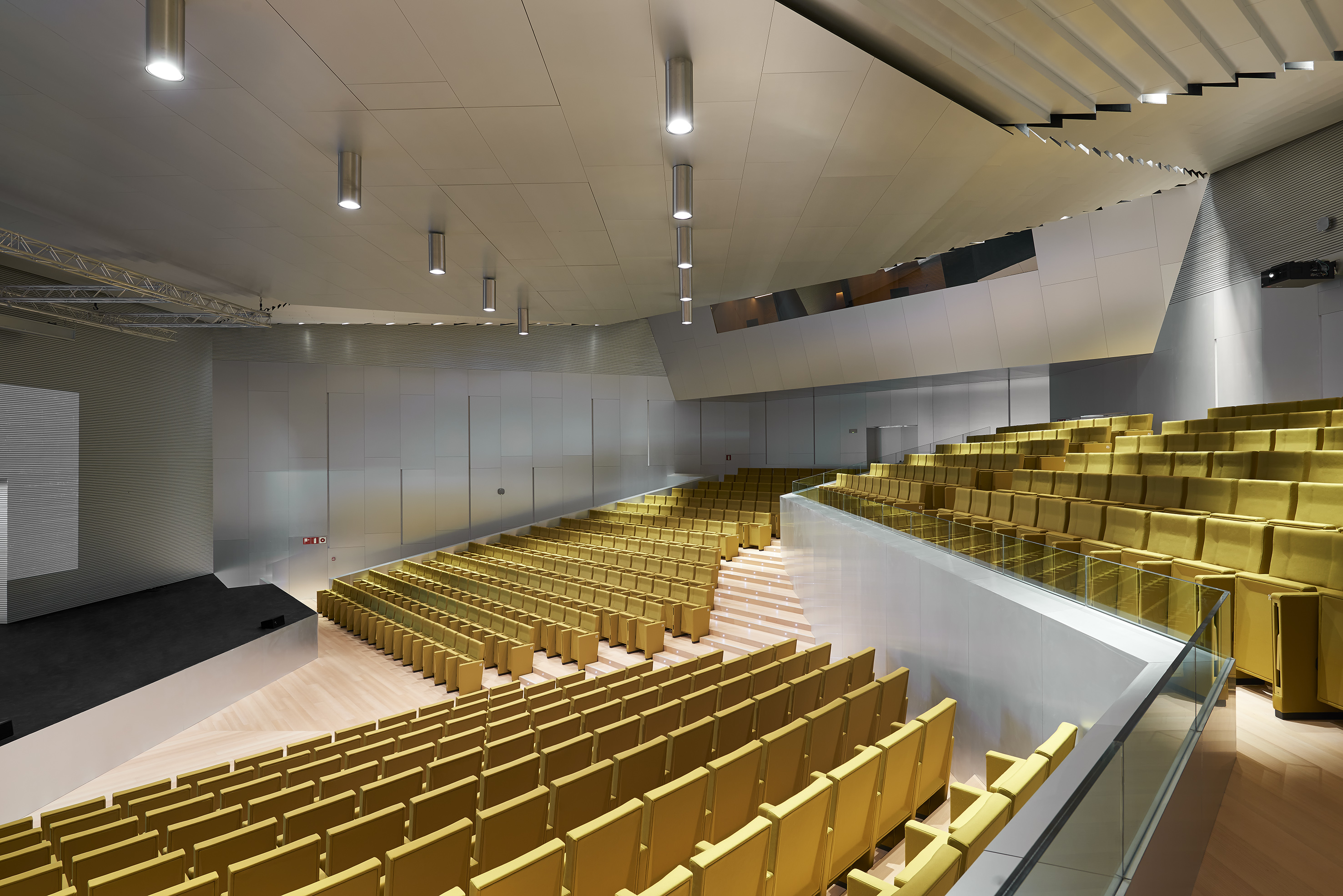 Modern auditorium with rows of yellow seats, large stage, and sleek design.