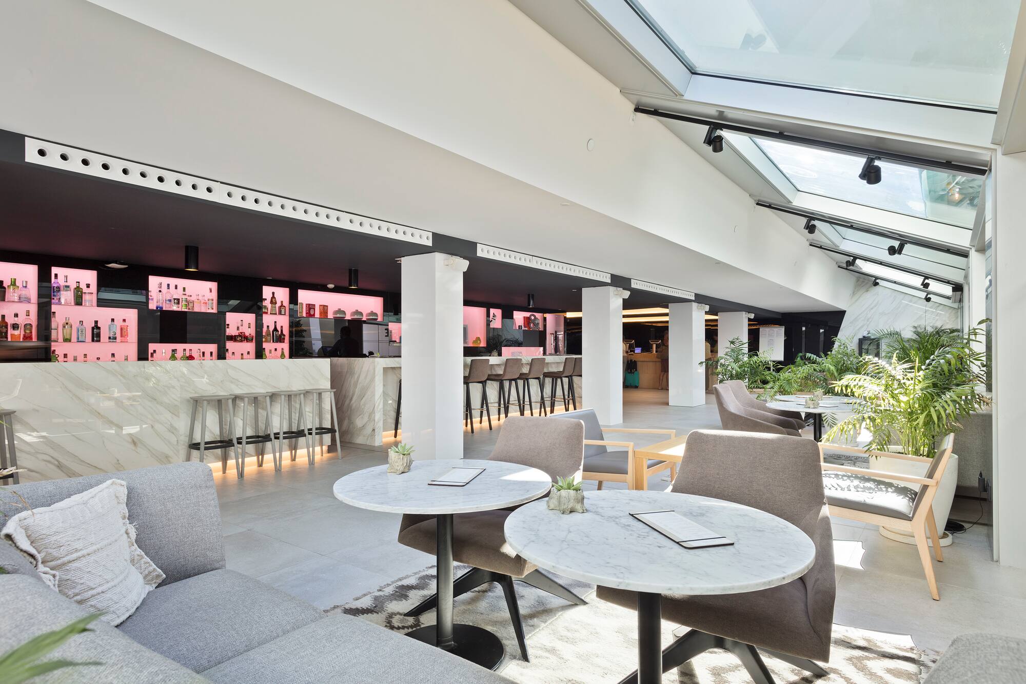 Modern hotel lounge bar with marble counters, stylish seating, and skylight.