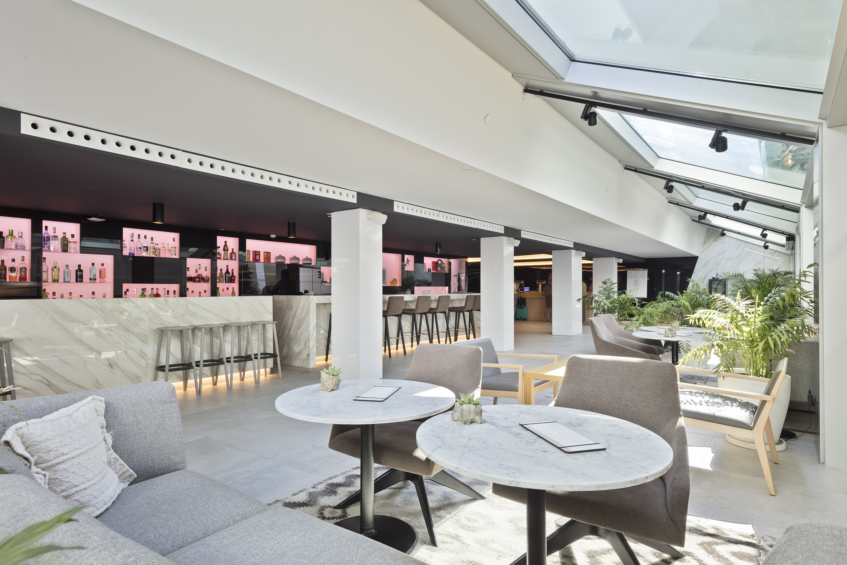 Modern hotel lounge bar with marble counters, stylish seating, and skylight.