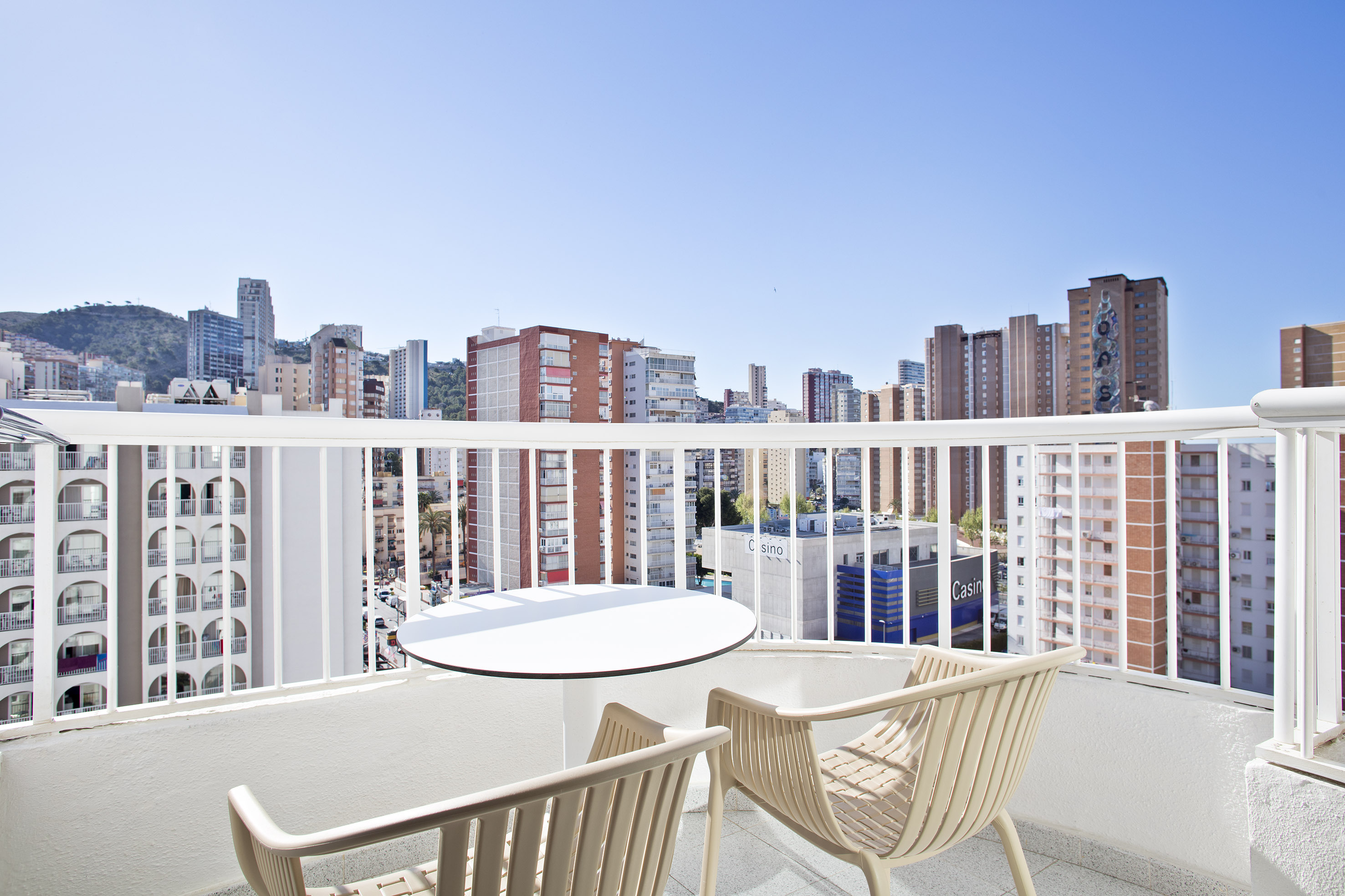 Balcony with table, chairs, and high-rise city skyline. Urban view, clear sky.