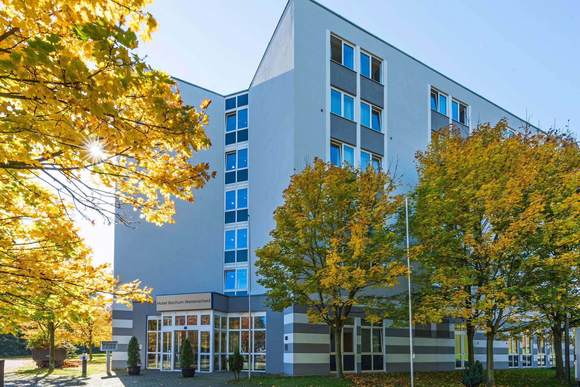 Hotel Bochum Wattenscheid in autumn, modern building with golden leaves.