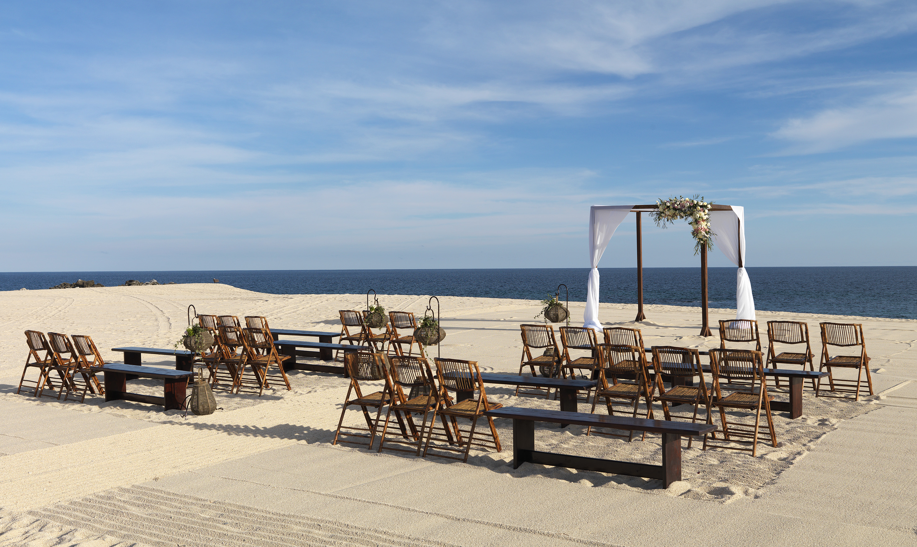 Beach wedding ceremony setup with floral arch, chairs, and ocean view.
