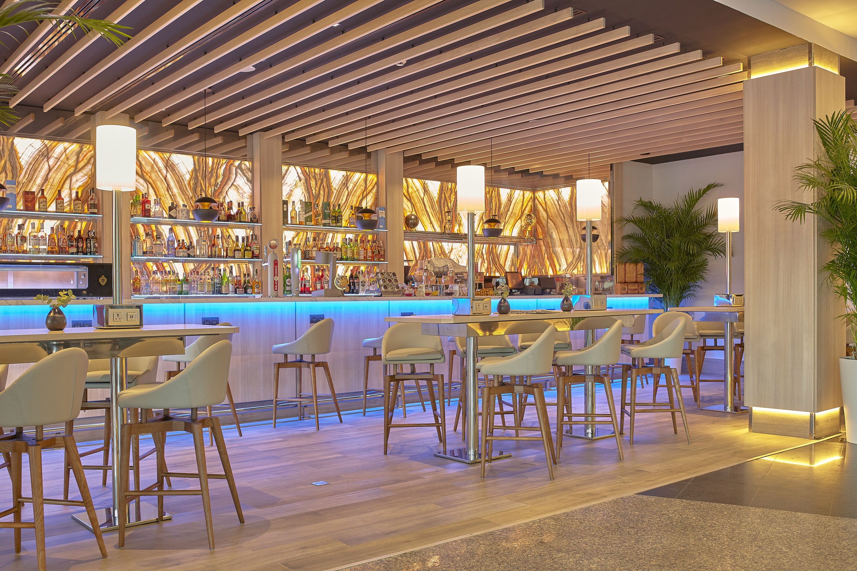 Modern hotel bar with blue LED lighting, backlit liquor shelves, and bar stools.