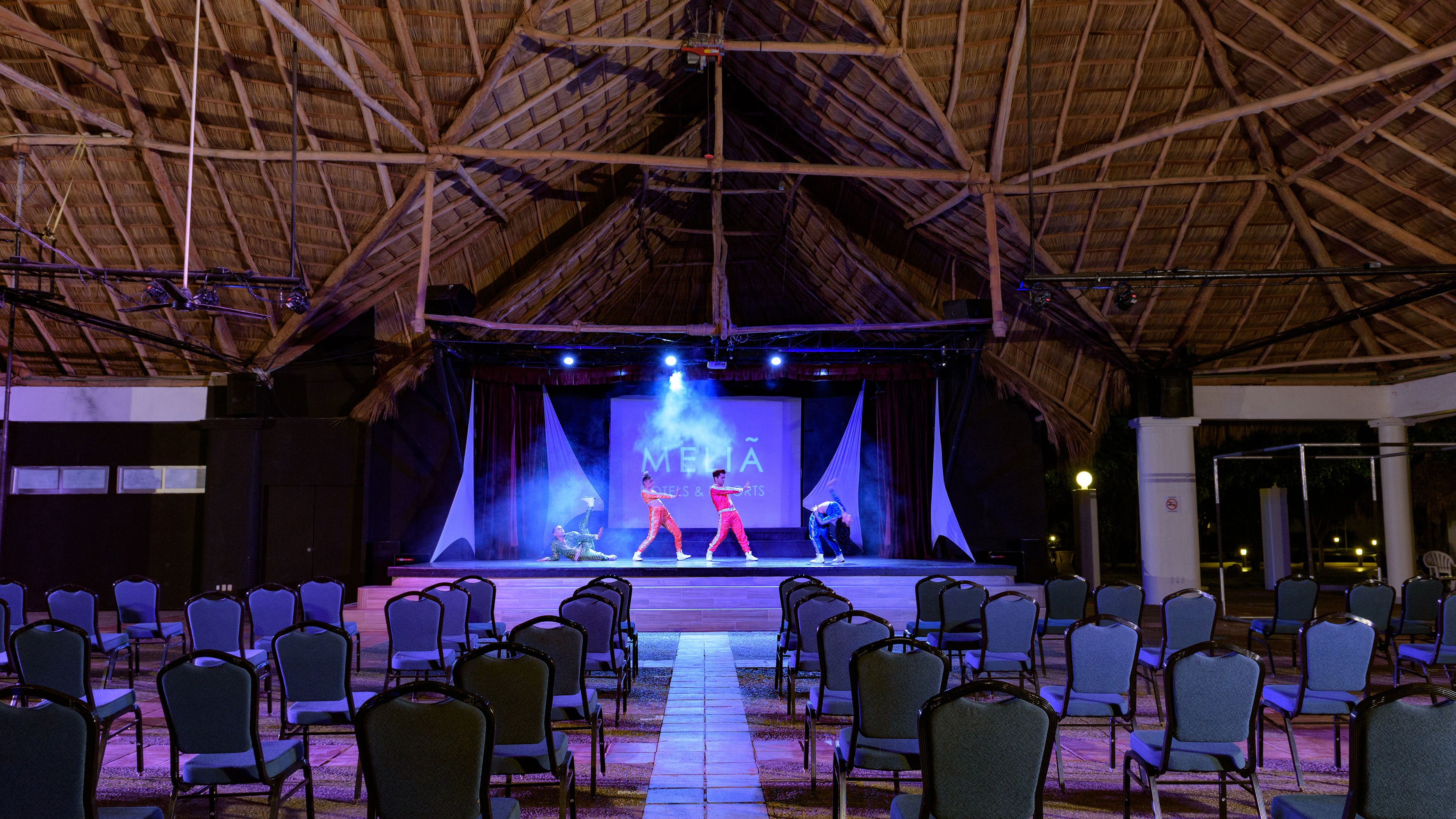 Dancers perform on stage at Meliá Hotels & Resorts with thatched roof.