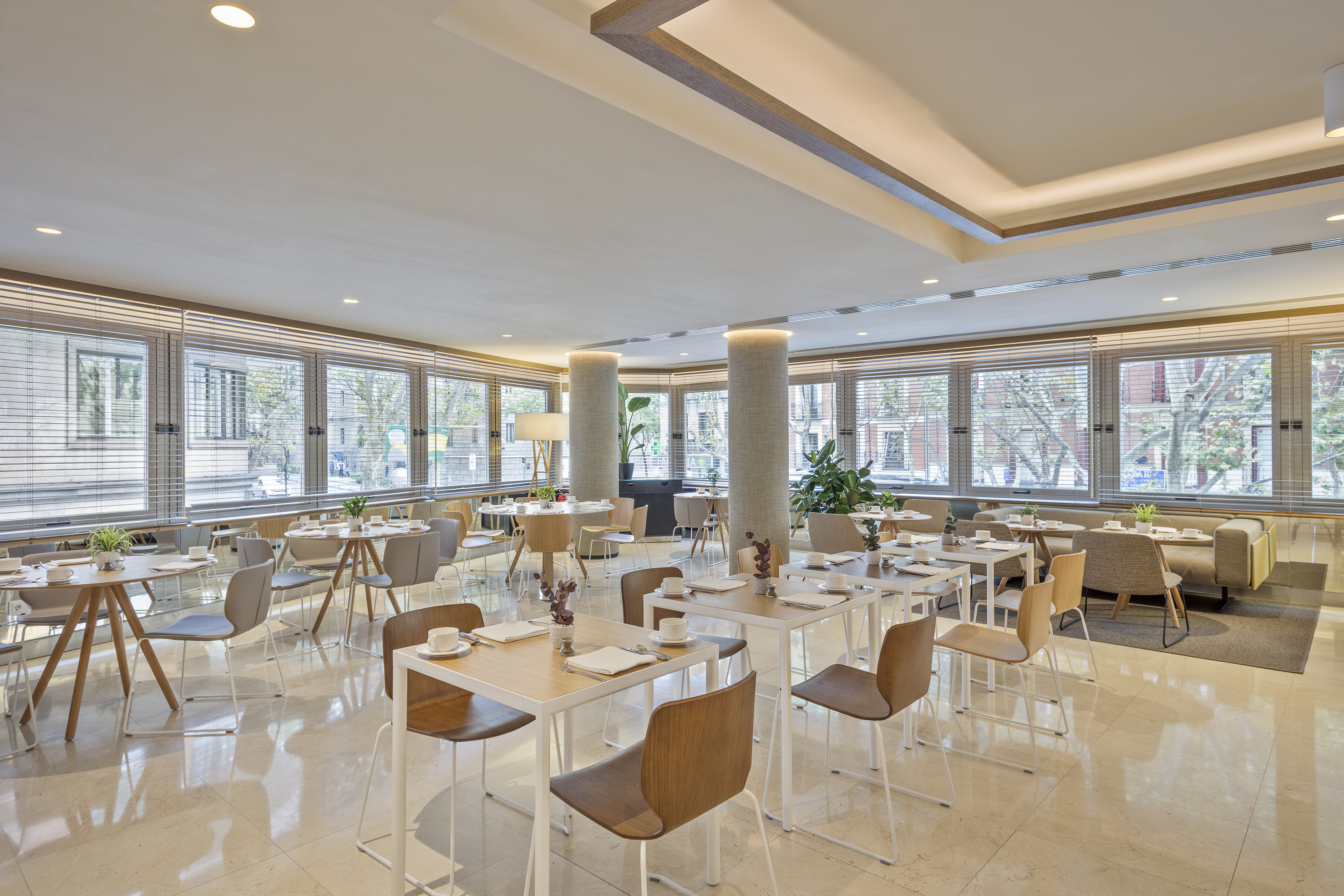 Bright, modern hotel dining area with tables, chairs, and large window views.
