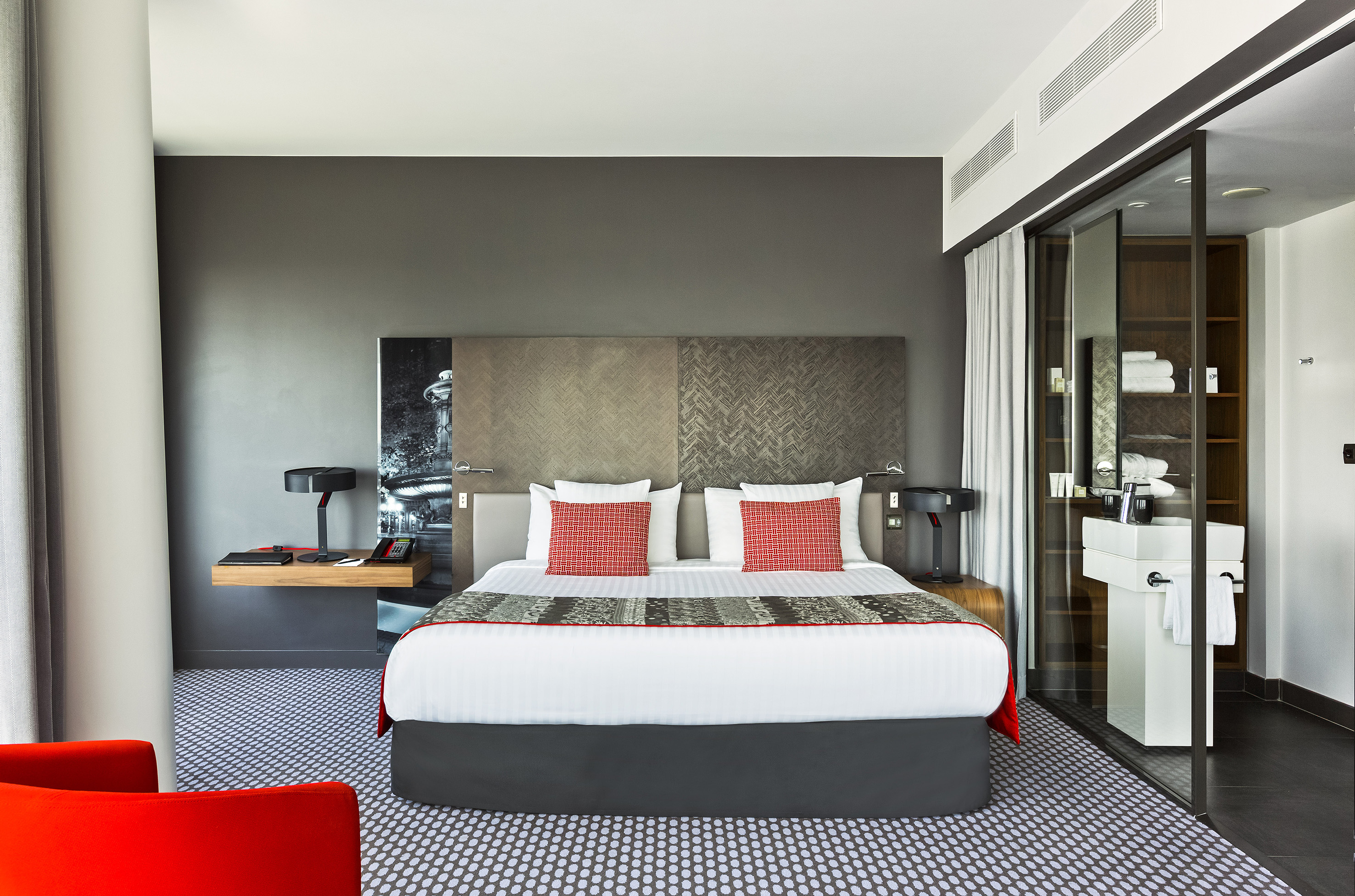 Modern hotel room with king bed, red pillows, and integrated glass bathroom.