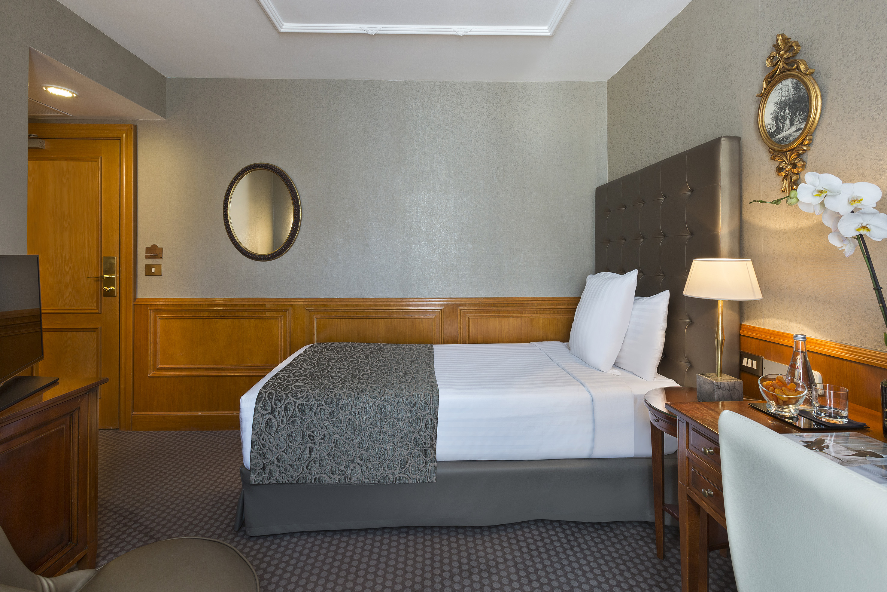 Luxury hotel room with queen bed, wooden paneling, and elegant furnishings.