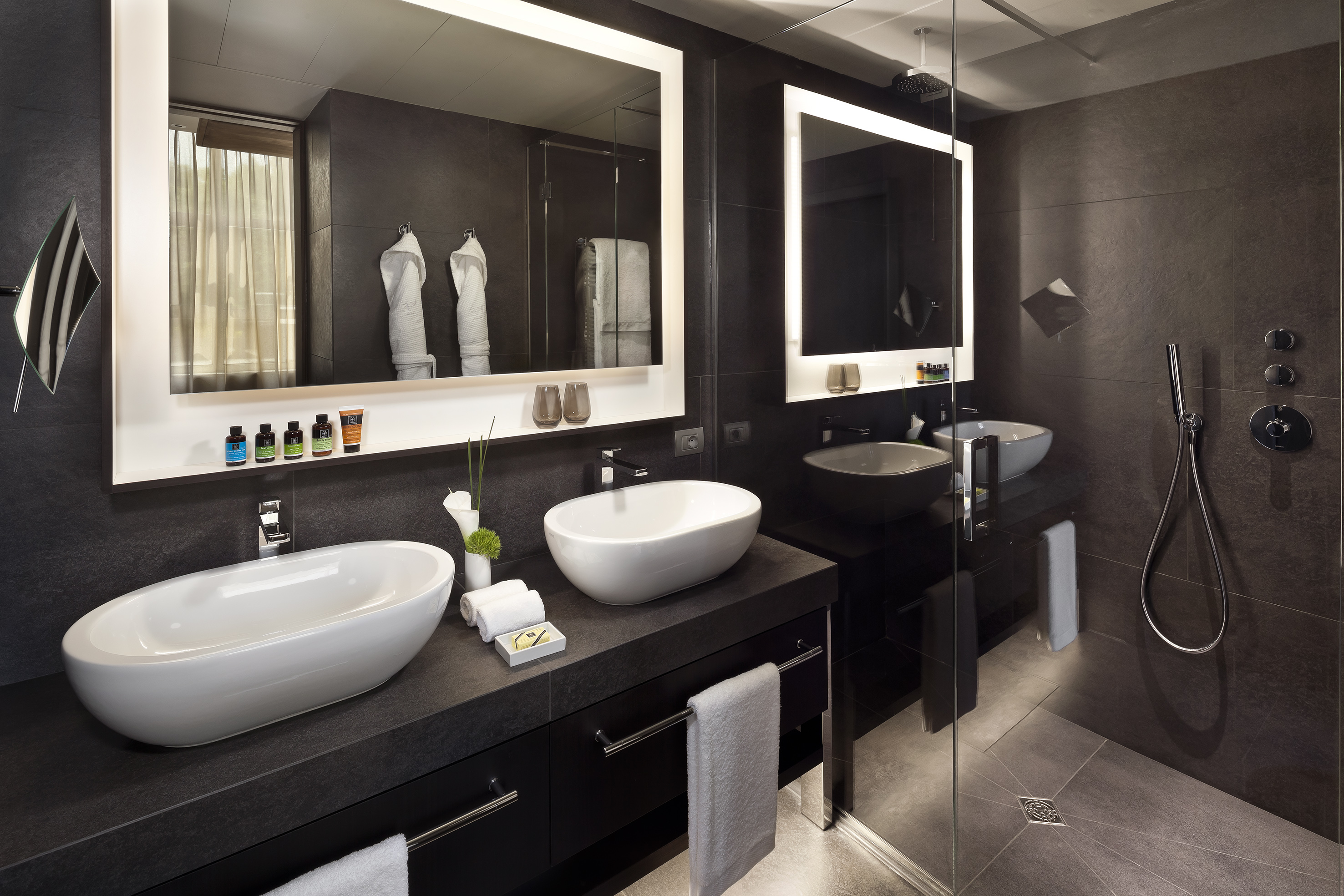 Modern hotel bathroom with dual sinks, backlit mirrors, and glass shower.