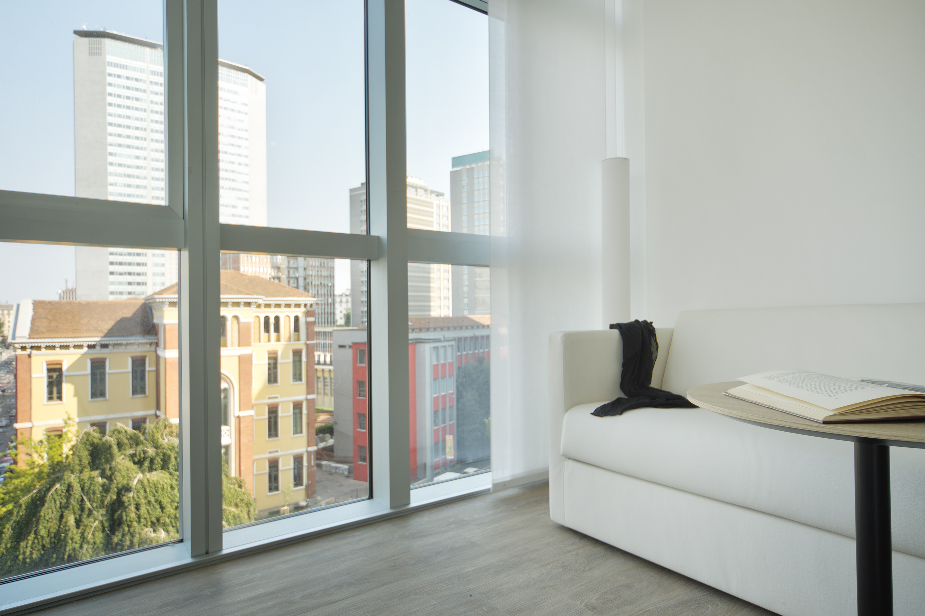 Modern apartment with white sofa, large window, and urban city view.