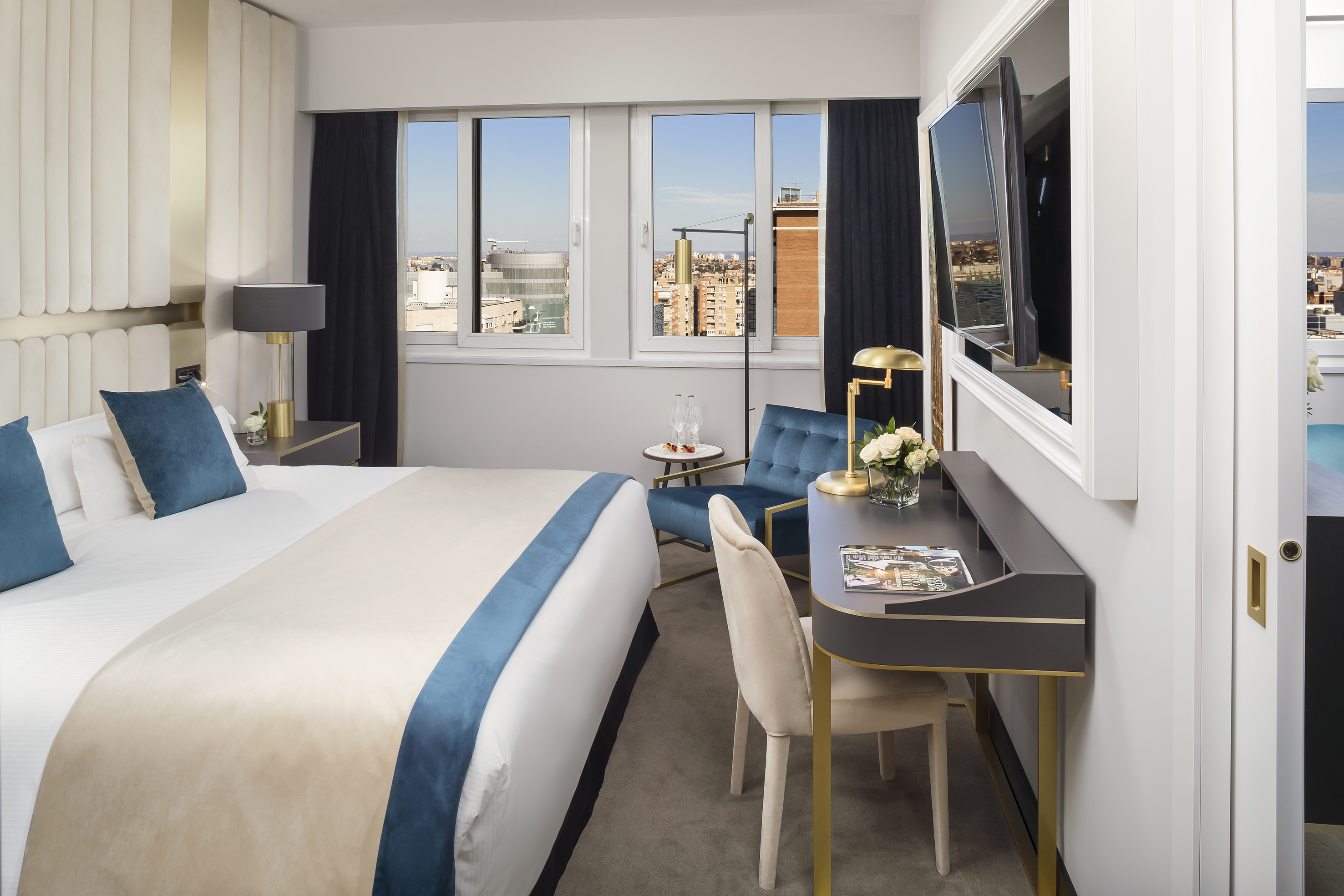 Luxurious hotel bedroom with city view, king bed, desk, and modern decor.