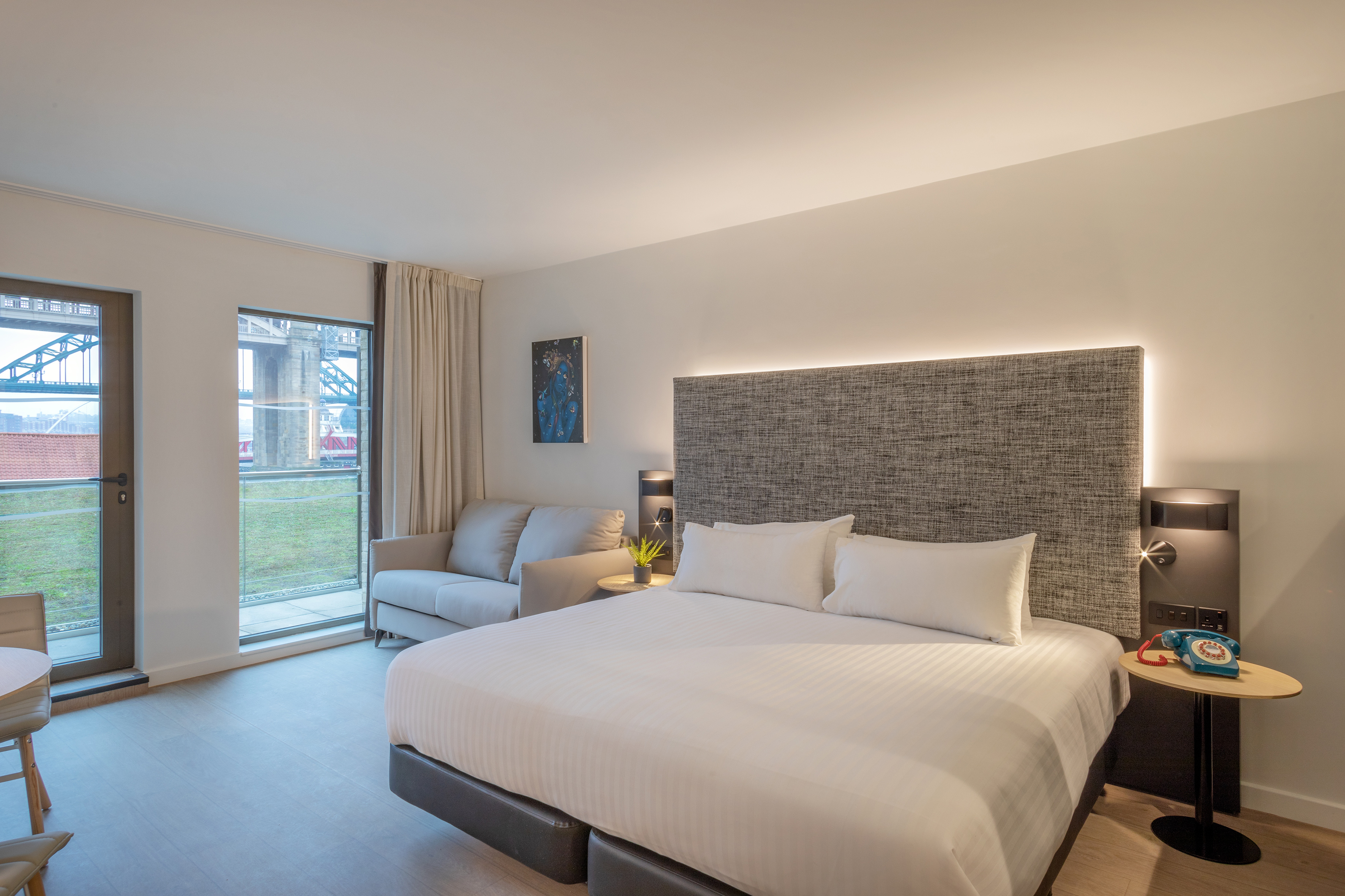 Modern hotel room with queen bed, sofa, and scenic bridge view.