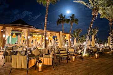 a patio with tables and chairs and umbrellas and palm trees