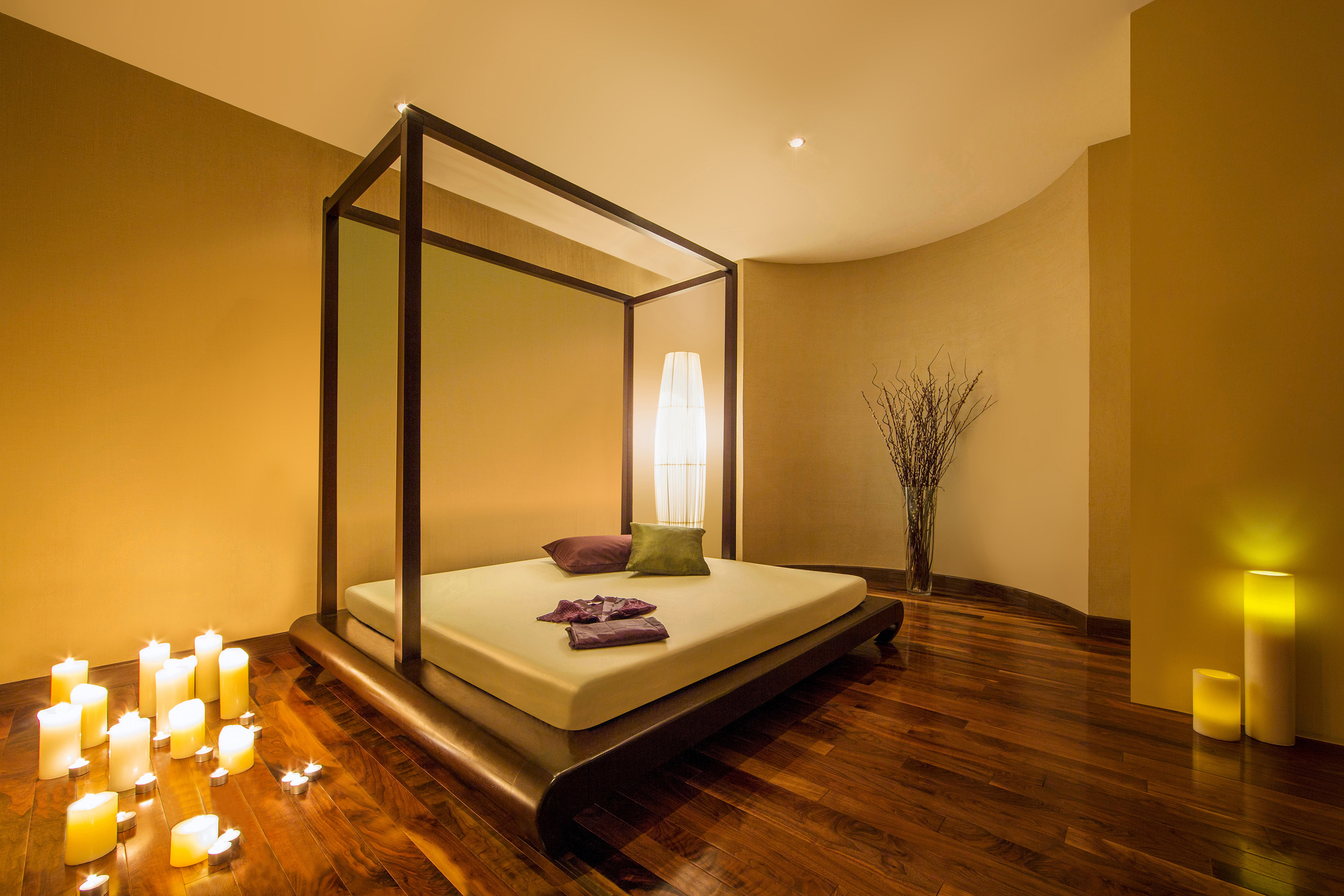 Spa room with platform bed, lit candles, warm lighting, and wooden floor.
